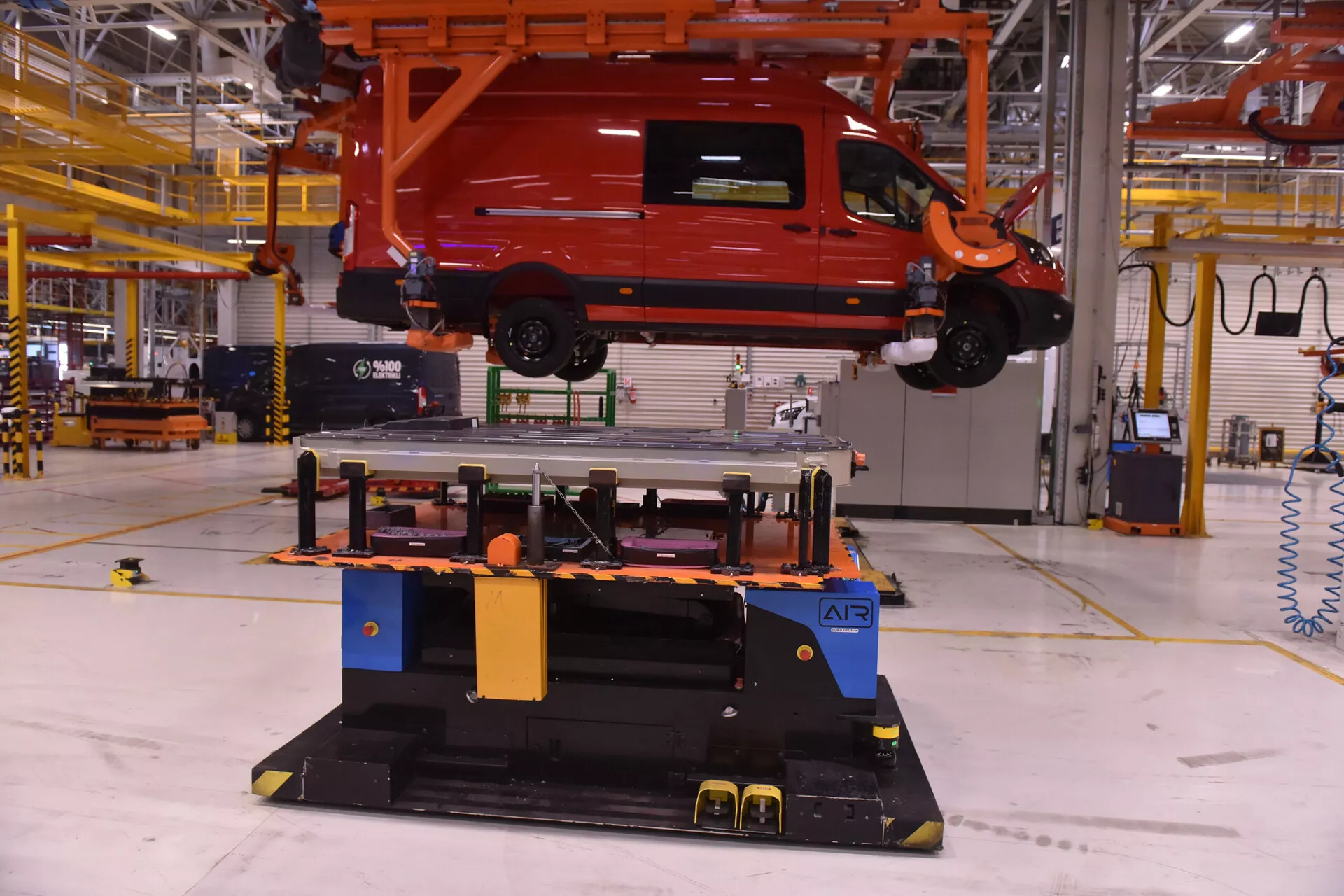 Furgão comercial Alfa-Romeo Stelvio 2017 suspenso por um sistema de manuseio aéreo em uma instalação de fabricação, mostrando tecnologia na montagem de veículos e automação de linhas de produção