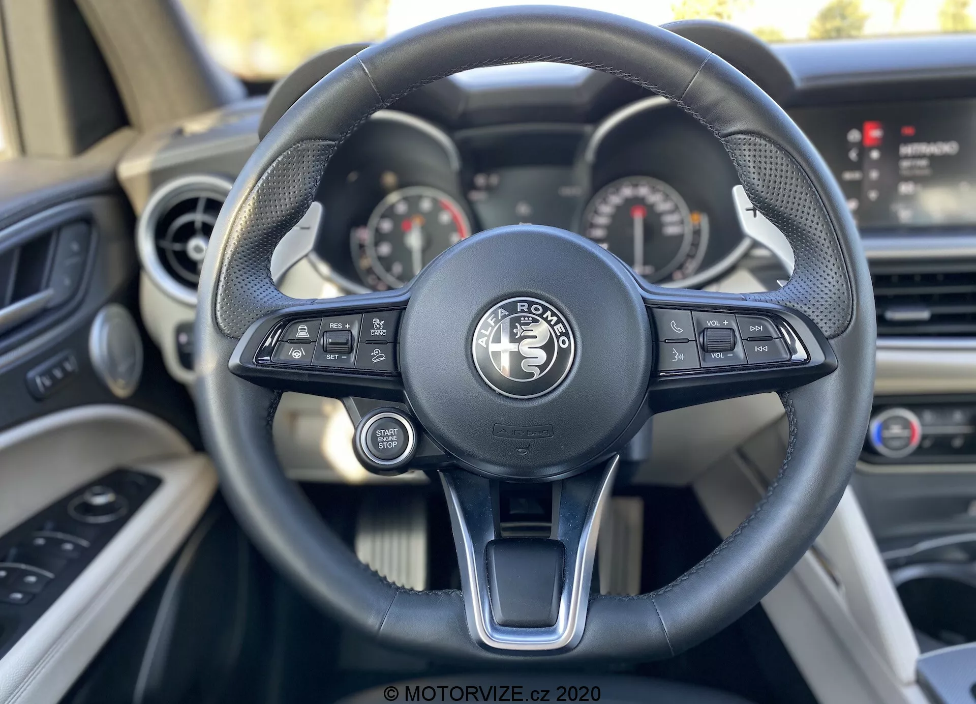 Vista de close-up da perspectiva do motorista a partir do assento do motorista em um veículo Land Rover, destacando o volante moderno de três raios com controles de tecnologia integrados e o painel sofisticado com mostradores analógicos e uma tela digital.