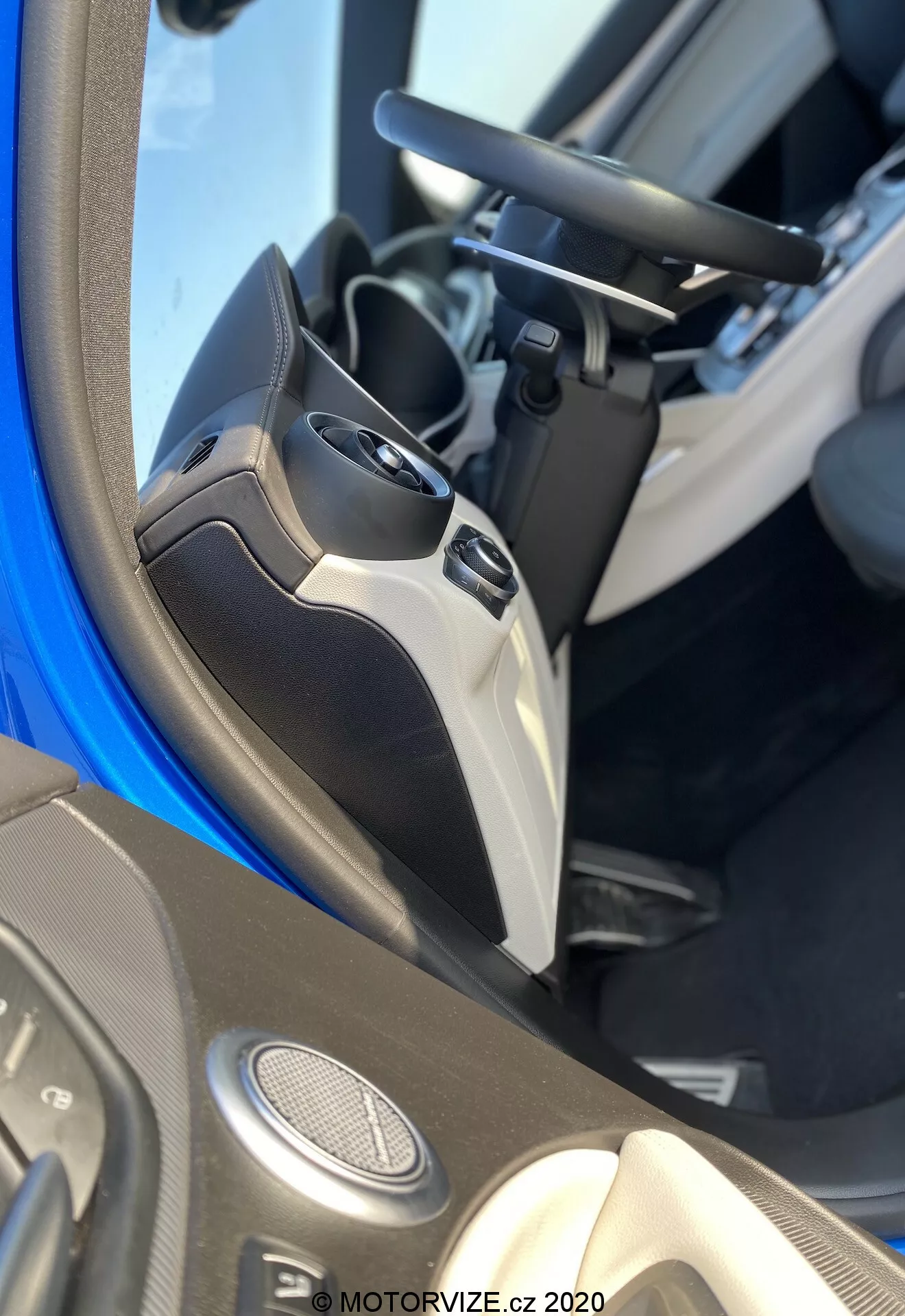 Close-up do interior do Alfa Romeo Stelvio 2017, focando no painel da porta do motorista. A foto captura a metade inferior da porta e parte do assento do motorista, mostrando várias características tecnológicas. O painel inclui alto-falantes montados na porta, sugerindo um sistema de áudio avançado, controles de vidros elétricos com vários botões para funcionalidade de um toque, e um controle de ajuste do espelho lateral elétrico. A maçaneta da porta, integrada no design, também é visível. Os materiais utilizados indicam um nível específico de acabamento ou um pacote de interiores, com um bolso de armazenamento na parte inferior. A imagem está marcada com 'MOTORVIZE.cz 2020'.