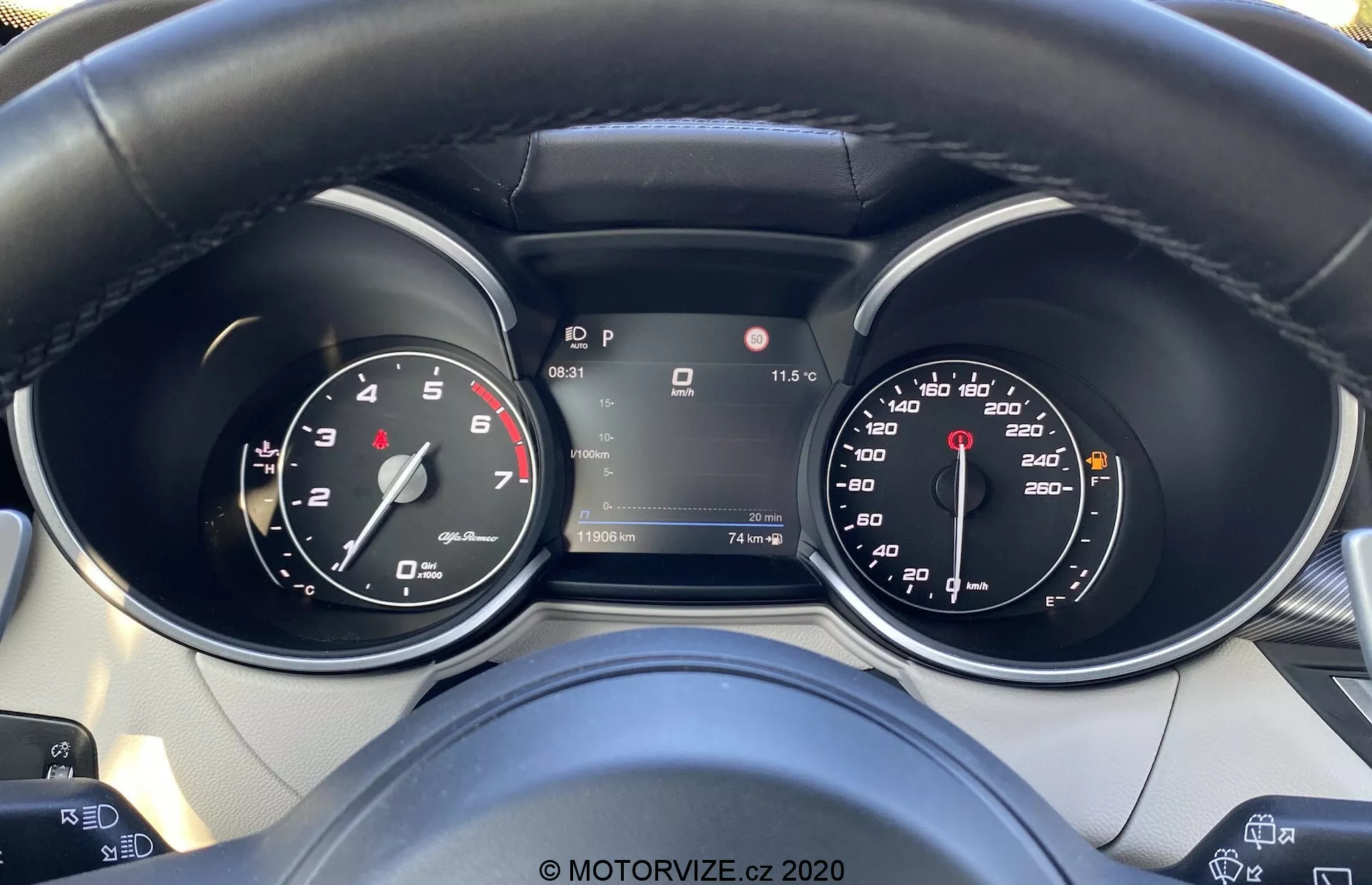 Vista detalhada do painel de instrumentos do Alfa-Romeo Stelvio 2017 a partir da perspectiva do motorista, mostrando o velocímetro, o tacômetro e um display digital central em modo Park. O volante apresenta botões de controle, sugerindo comodidades tecnológicas avançadas, e o painel inclui indicadores de temperatura, assistência de manutenção de faixa e outras informações de condução.