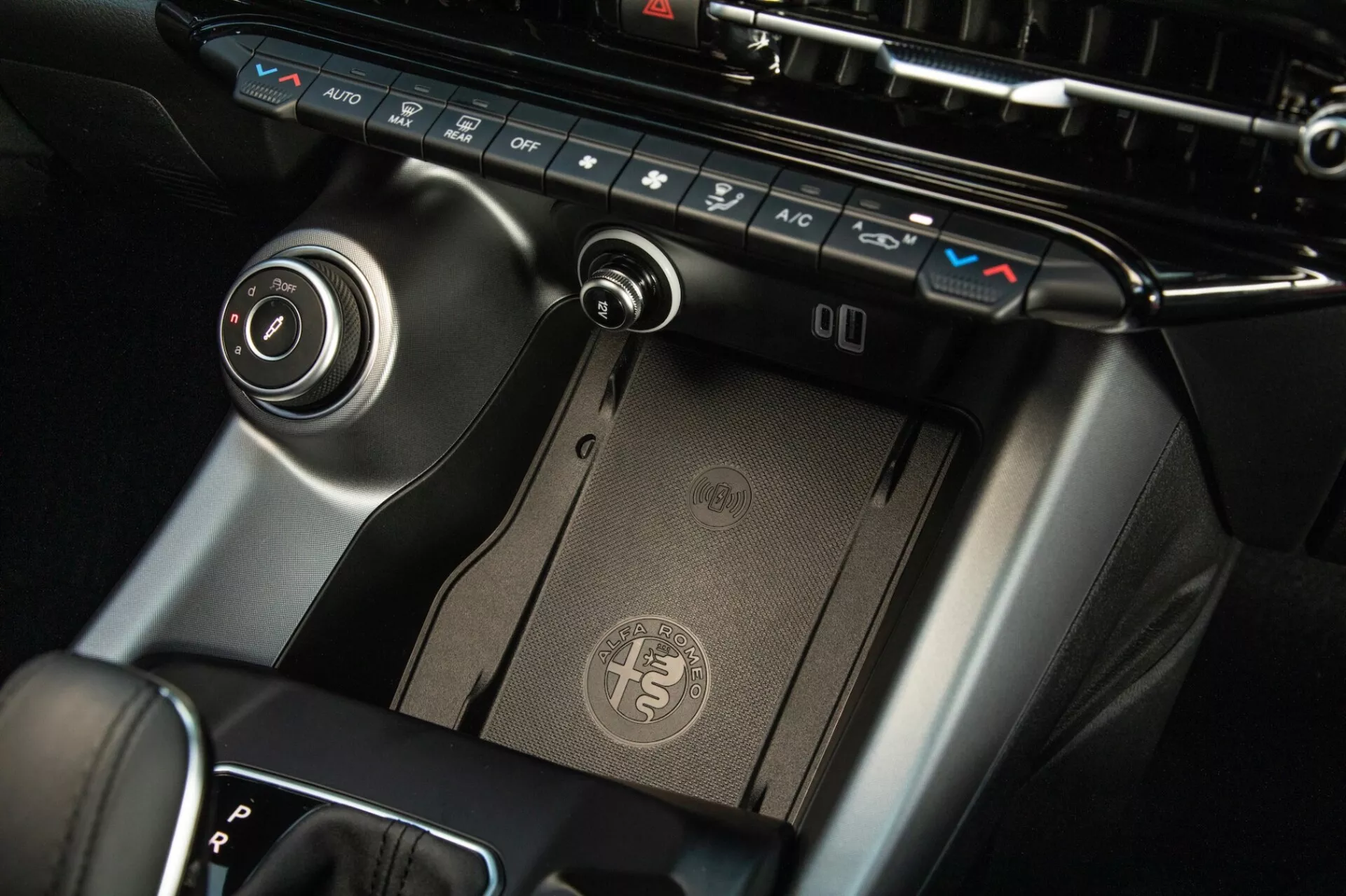 Visão detalhada do console central do Alfa Romeo Tonale 2022, mostrando painel de controle climático, almofada de carregamento sem fio, alavanca de câmbio e dial de controle de infotenimento com acabamento premium e design moderno.