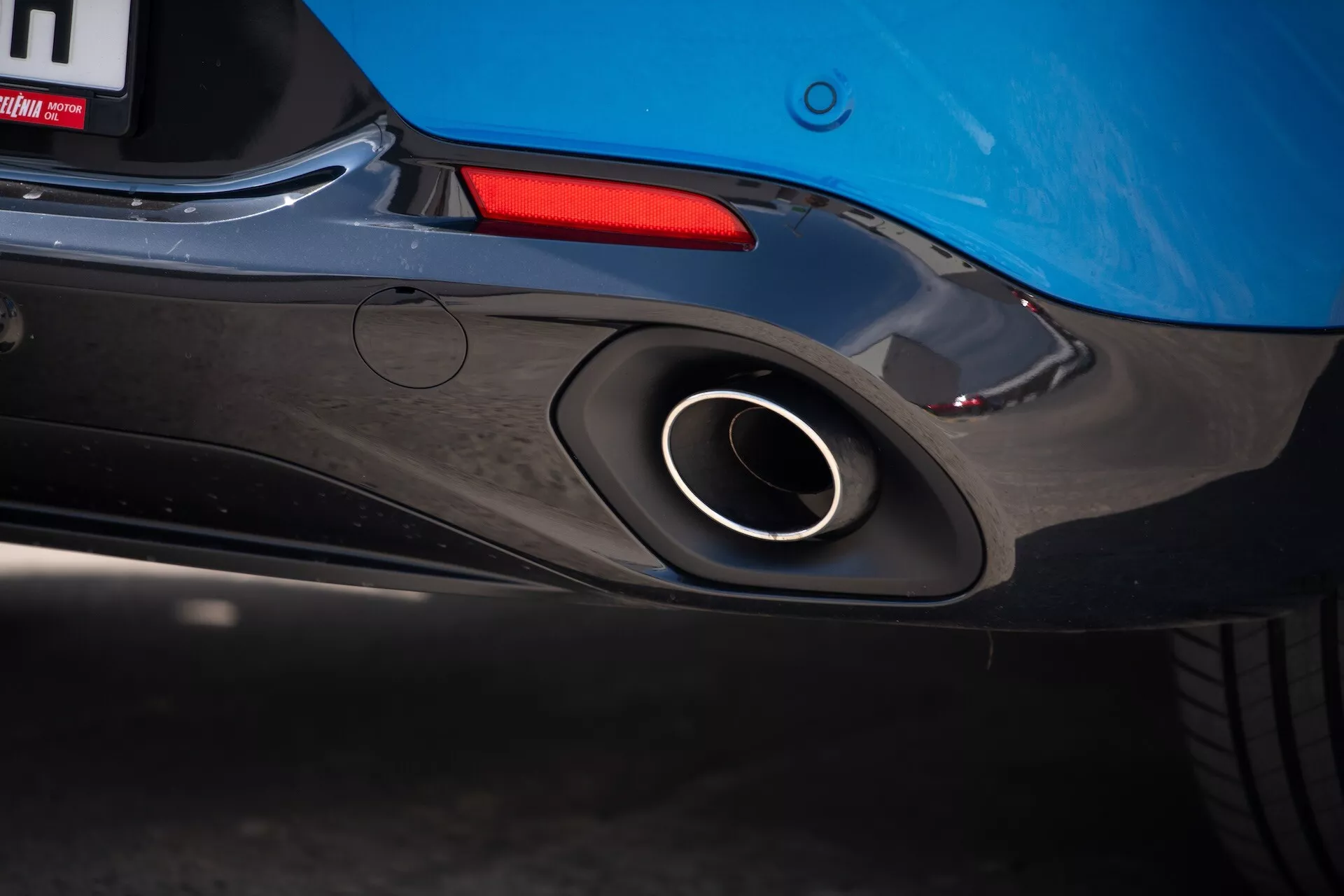 Vista de perto da seção traseira do Alfa Romeo Tonale 2022 destacando o cano de escape esportivo, design aerodinâmico do para-choque traseiro e cor azul do corpo com um vislumbre da luz traseira