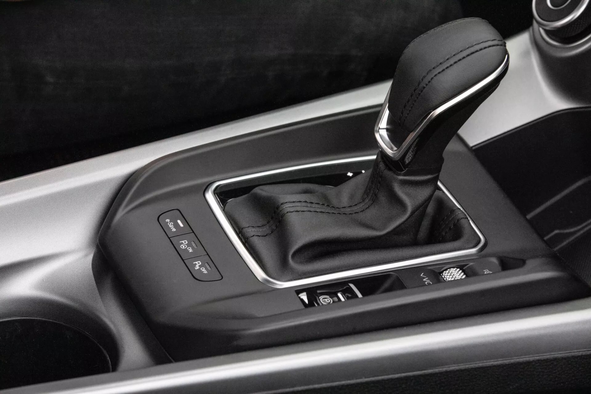 Vista detalhada do interior do console central do Alfa-Romeo Tonale 2022 com alavanca de mudança de transmissão automática em alojamento prateado com indicadores de seleção de marcha, botões de controle integrados e acabamento de alta qualidade