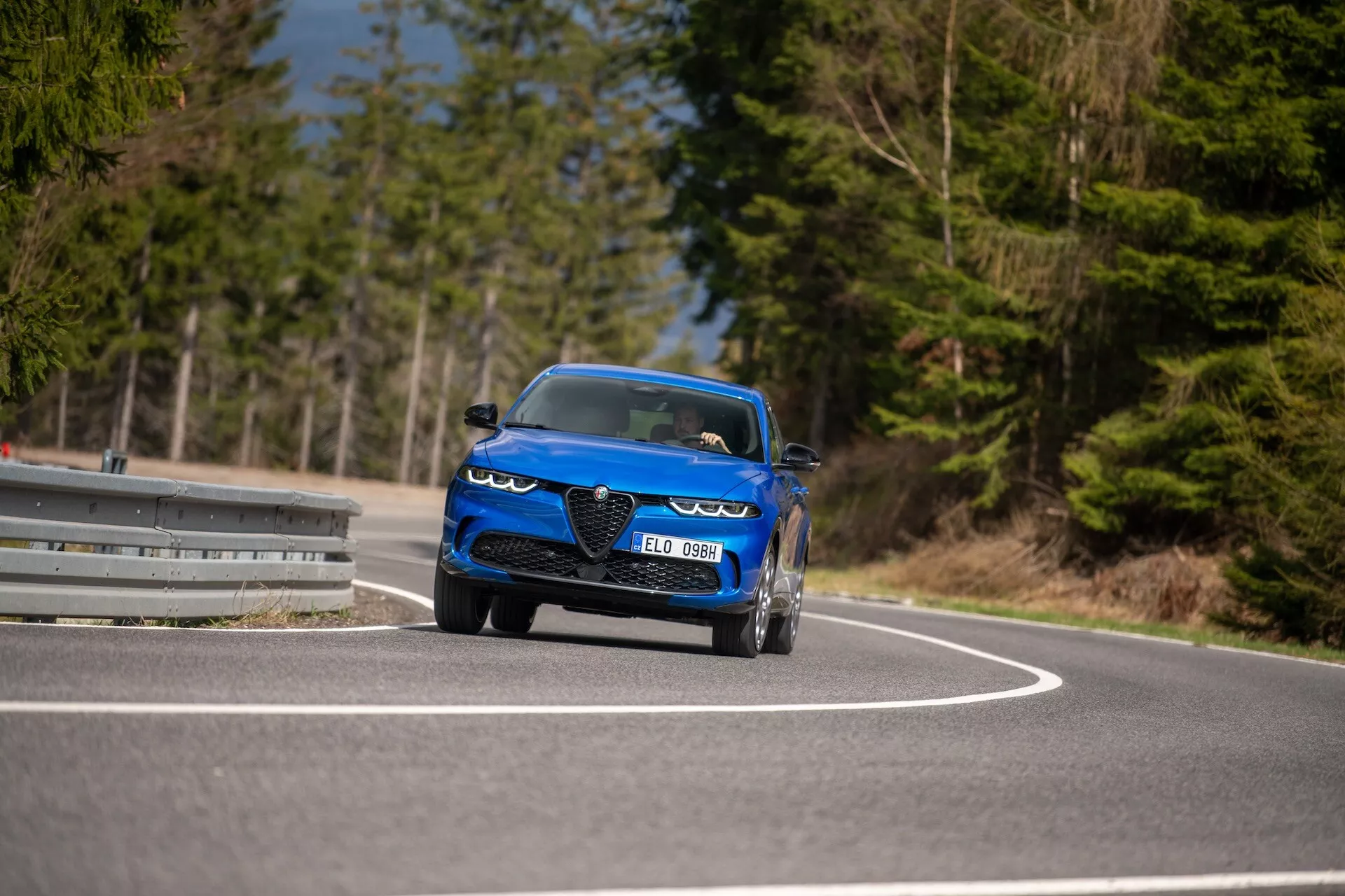 Alfa-Romeo Tonale 2022 em movimento numa estrada curva, exibindo seu design dinâmico, faróis LED, entradas de ar, estilo conversível esportivo e características de luxo de uma perspectiva frontal de três quartos em ângulo baixo