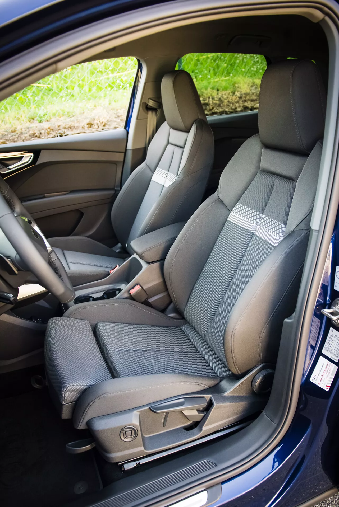 Interior do Audi Q4 e-tron 2021 mostrando o assento dianteiro do lado do passageiro com estofamento em dois tons, costura detalhada, controles de ajuste elétrico e cinto de segurança, junto com uma visão do assento traseiro divisível e rebatível e características tecnológicas da cabine.