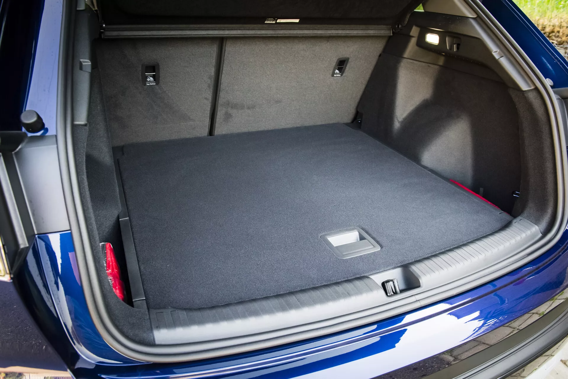 Vista da área de bagageira espaçosa e alcatifada do Audi Q4 e-tron 2021 com a tampa da mala aberta, mostrando soluções de armazenamento inteligentes e um vislumbre do seu exterior azul metálico com sensor de estacionamento visível