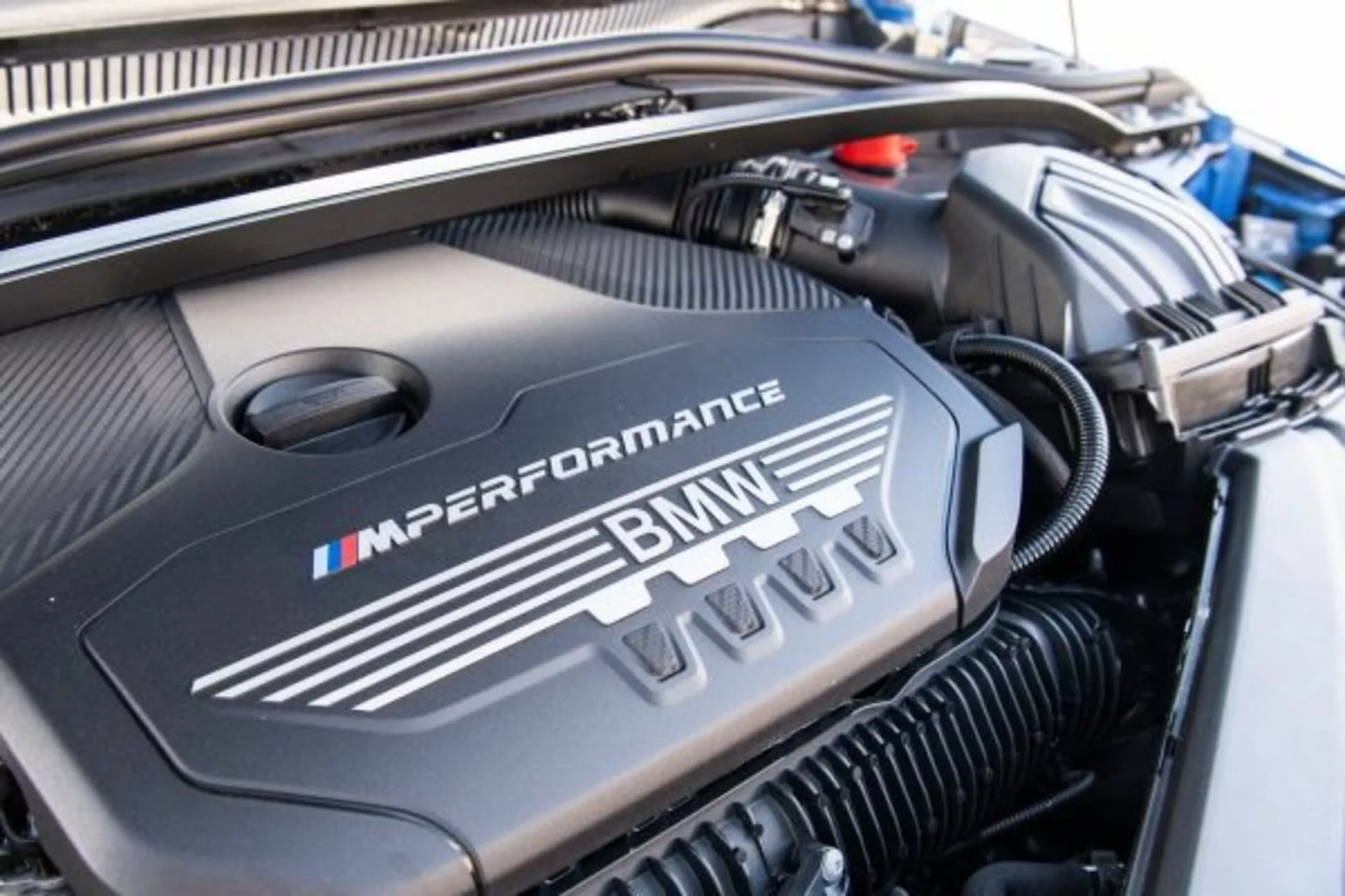 Visão de perto da tampa do motor BMW Série 1 M Performance 2019 mostrando o logotipo da BMW e as cores da divisão M em um compartimento do motor bem mantido