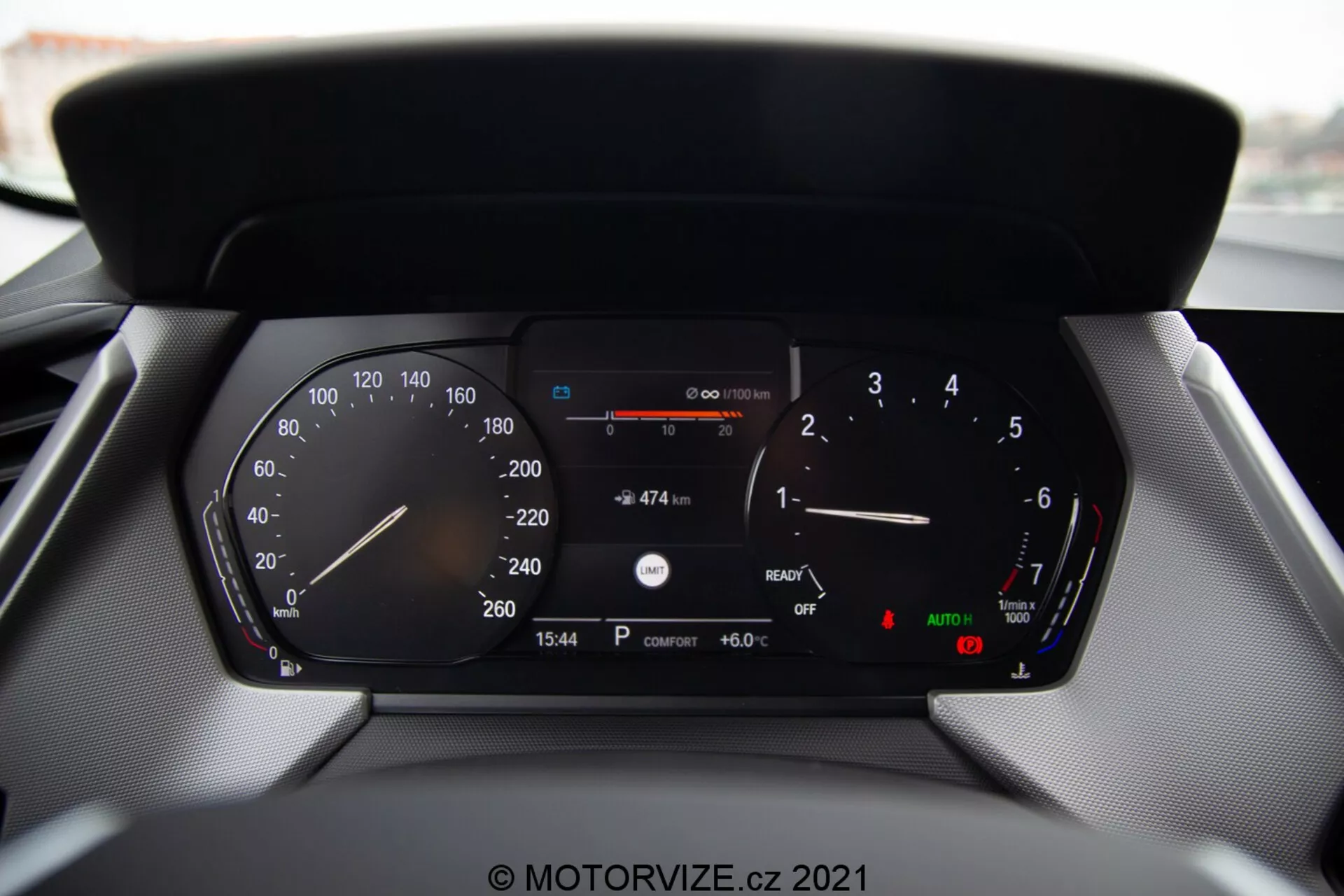 Visão aproximada do painel de instrumentos digital de um carro moderno BMW Série 1 2019 (BMW 116i), mostrando leituras detalhadas incluindo velocímetro, tacômetro, indicador de combustível, medidor de temperatura, leitura digital de velocidade, distância restante com o combustível atual, exibição do horário (15:54), temperatura externa (6.0°C) e indicadores de faróis automáticos e freio de estacionamento.