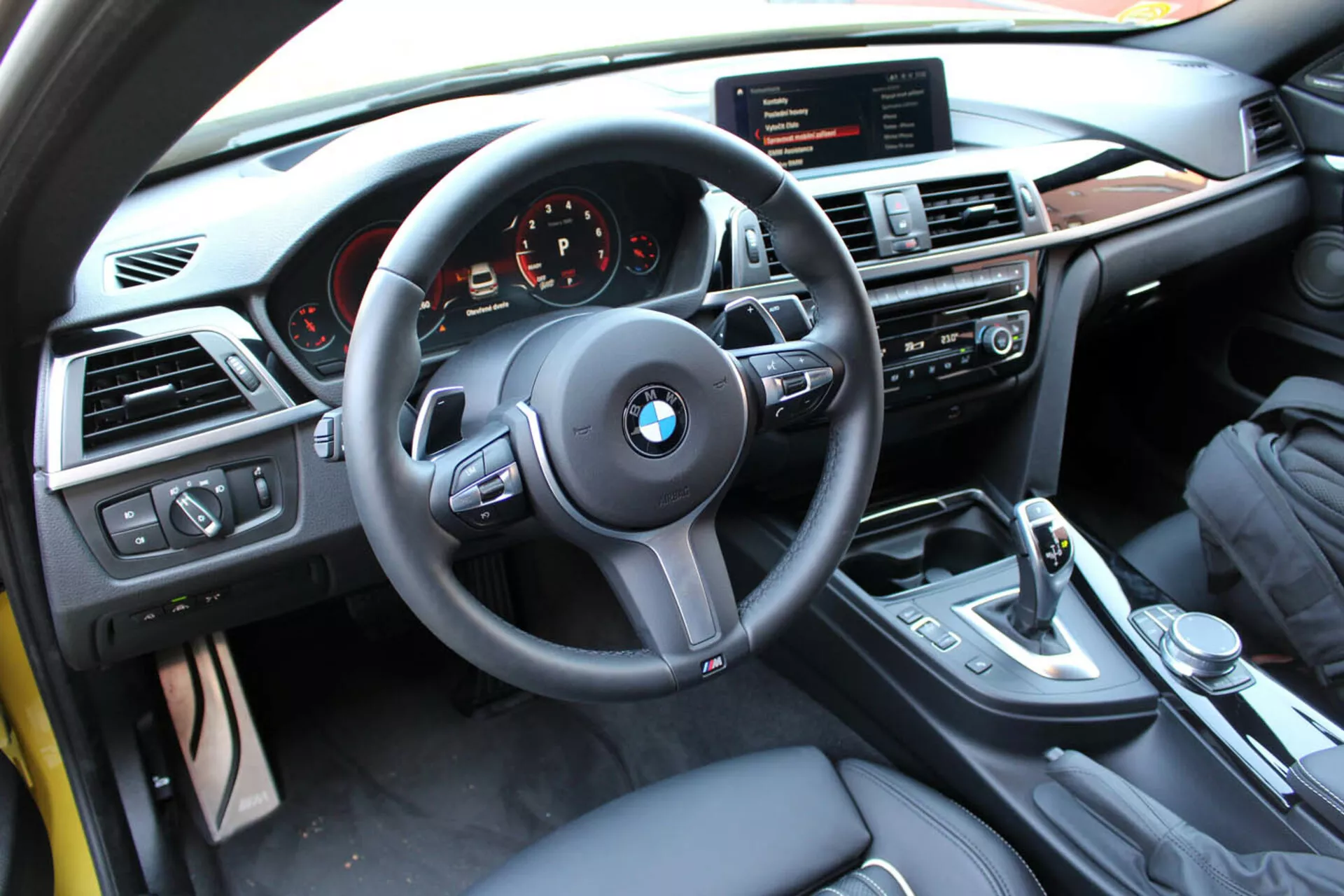 Vista do interior de um Coupé BMW Série 4 de 2013 a partir da perspectiva do condutor mostrando volante, painel de instrumentos, consola central com controles multimédia e de climatização, alavanca de mudanças, e acabamentos de luxo
