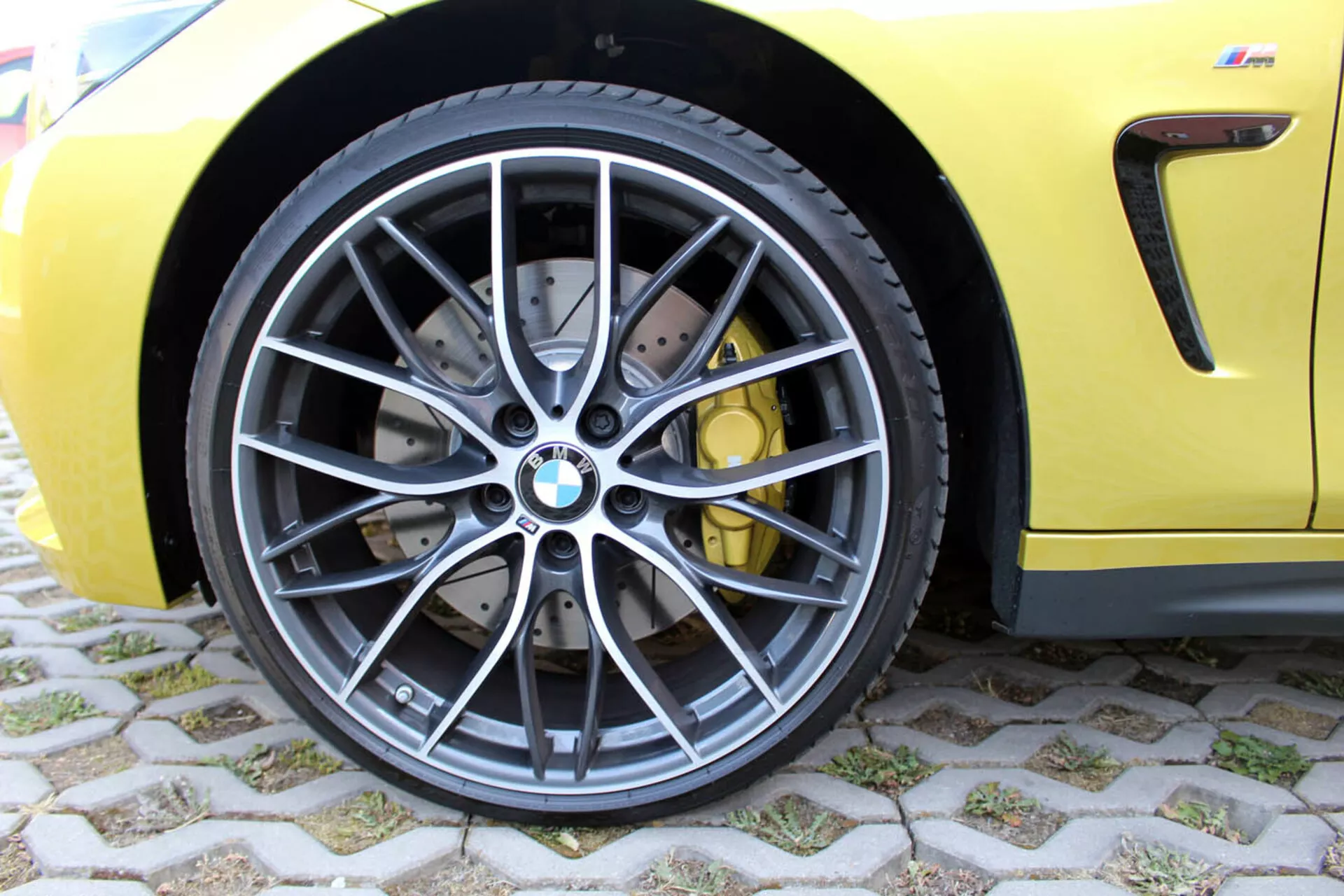 Vista detalhada da roda dianteira do BMW Série 4 Coupé 2013 com design de liga cinza escuro de vários raios, pneu radial sem câmara de baixo perfil, sistema de freio de alto desempenho com discos perfurados e pinças amarelas, em um corpo esportivo amarelo vibrante