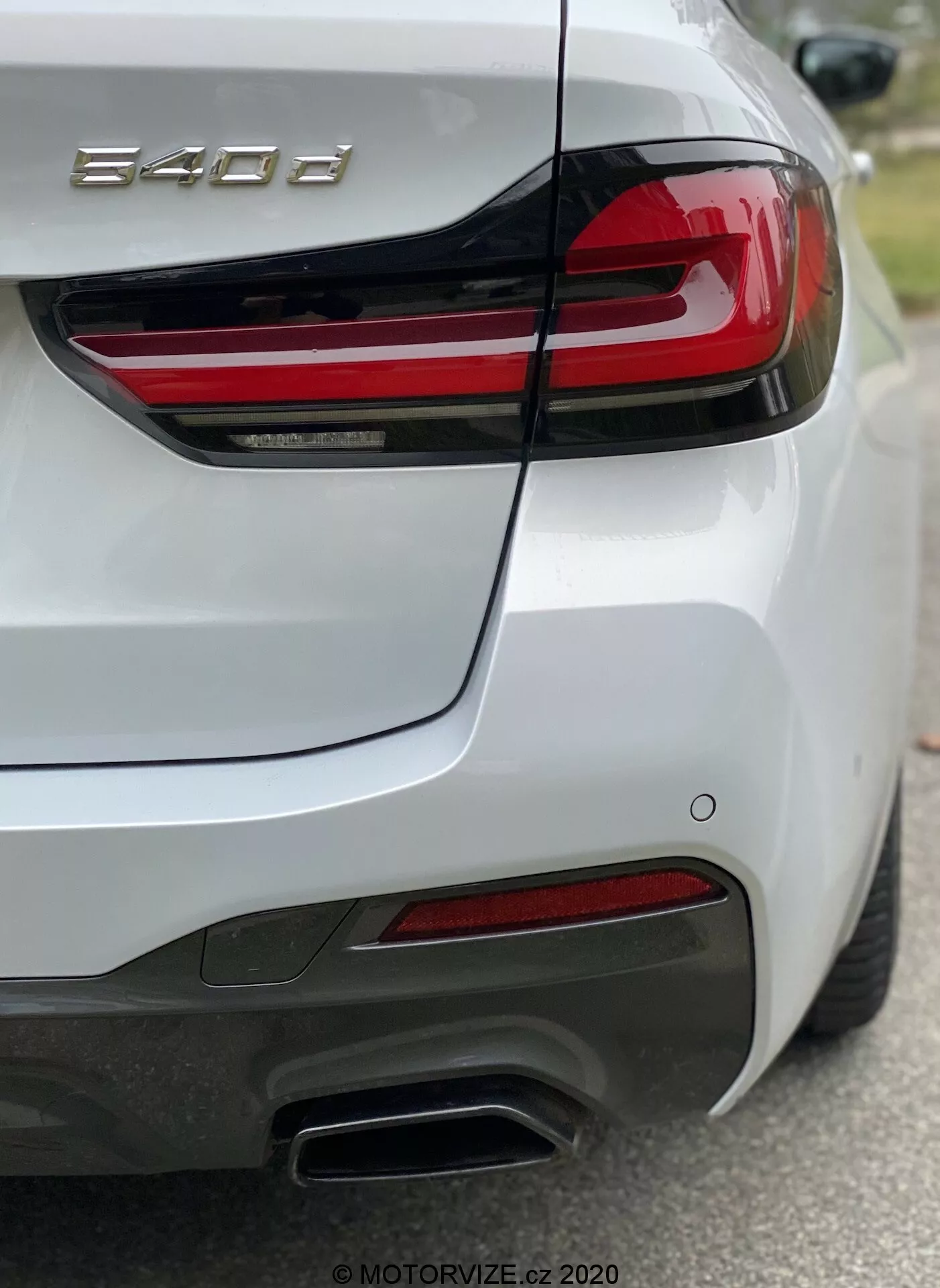 Parte traseira de um carro BMW Série 8 (840i), capturada a partir da vista do quarto traseiro direito, destacando a lanterna traseira direita com faixas LED vermelhas horizontais, tampa do porta-malas esculpida com spoiler integrado, para-choque traseiro com sensores, pontas de escape duplas metálicas no lado direito, refletores vermelhos e pintura branca brilhante. A foto foca na insígnia '840i', mostrando detalhes de design e características tecnológicas como iluminação e sistemas de assistência ao motorista.