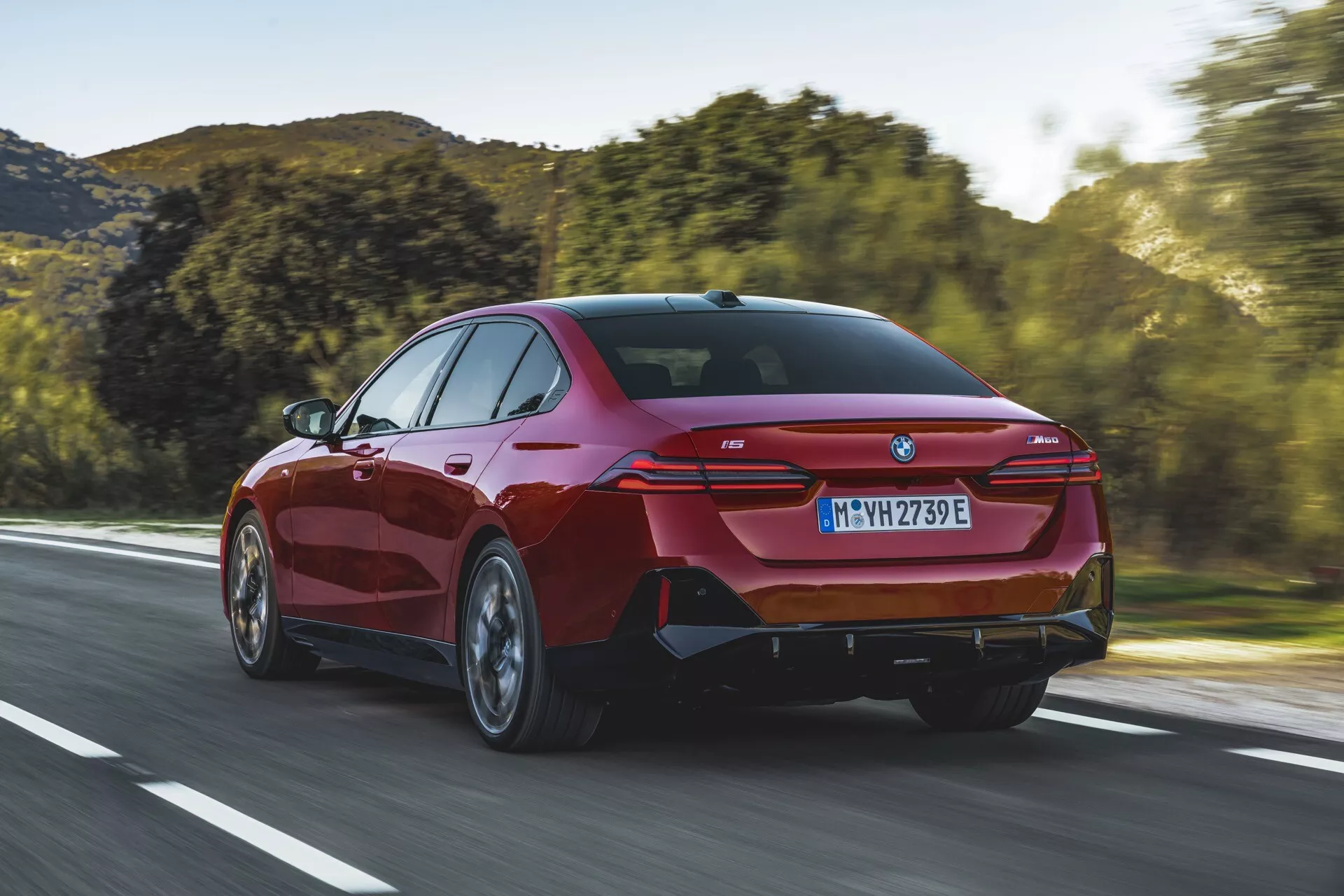 Sedan moderno BMW Série 5 (G60-G61) de 2023 dirigindo em uma estrada aberta, exibindo uma vista traseira de três quartos destacando as luzes traseiras elegantes, para-choque traseiro esportivo com portas de escape integradas, e uma silhueta distintiva tipo coupé.