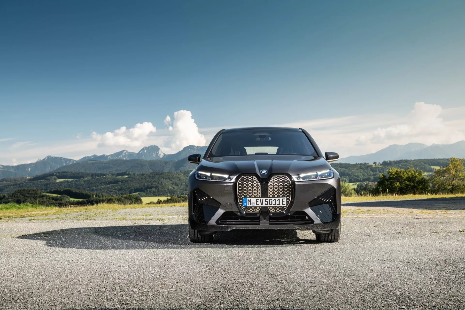 BMW iX (i20) 2021 fotografado de um ângulo frontal baixo, destacando seu design dominante com uma grade renal grande, faróis LED elegantes e entradas de ar orientadas ao desempenho contra uma paisagem montanhosa