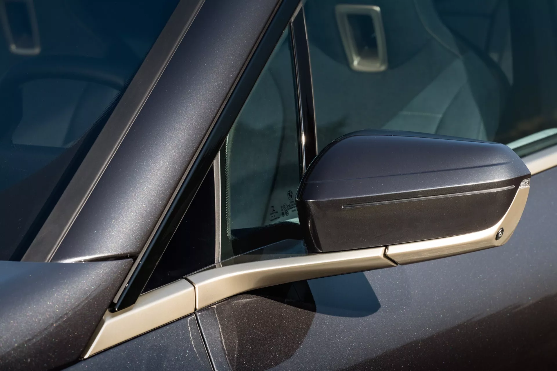 Vista detalhada de um BMW iX 2021 (i20) mostrando o design detalhado do espelho lateral na cor do carro com seta integrada, a elegante ponte de suporte aerodinâmico e uma parte da janela com vidro pequeno.