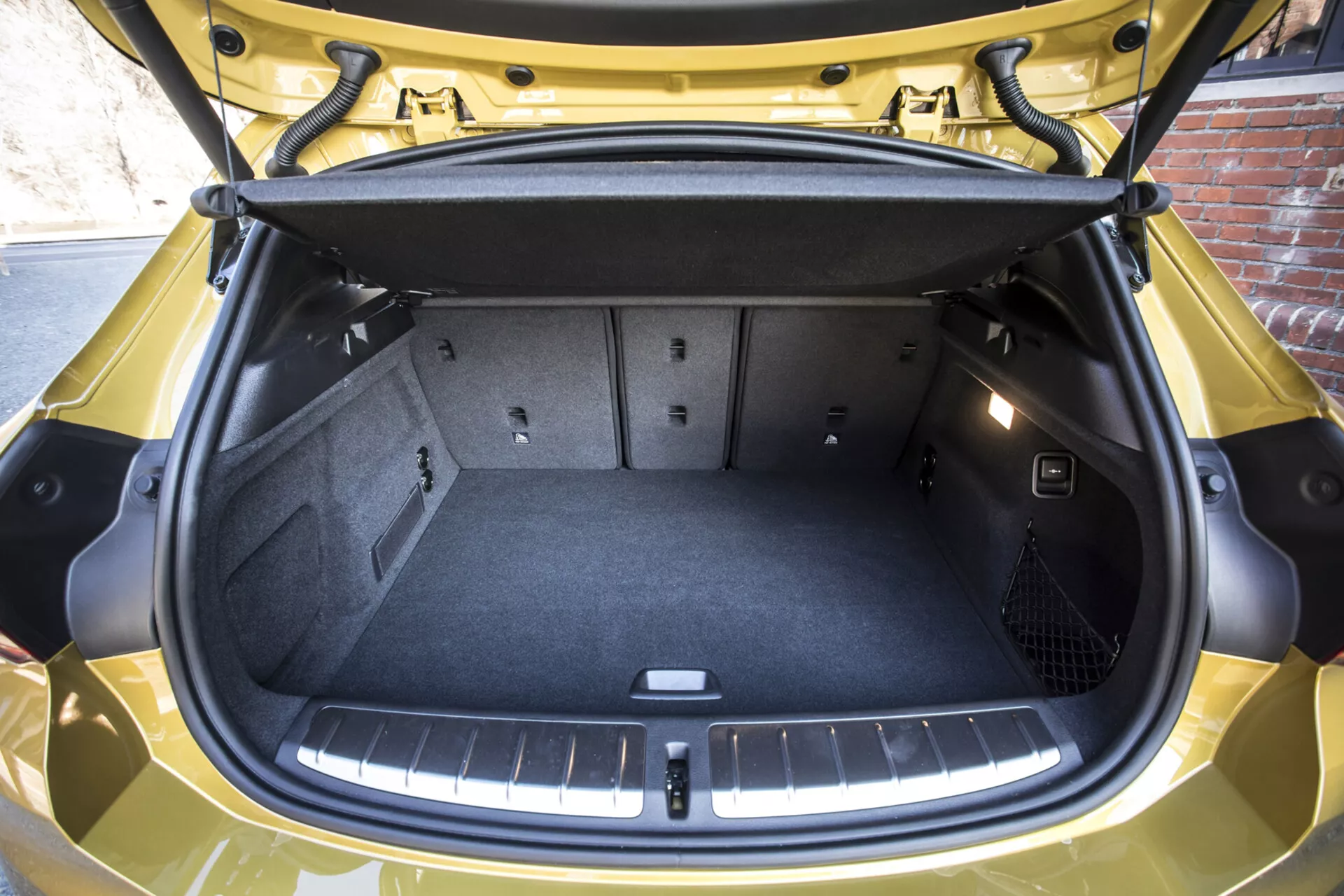 Visão detalhada do porta-malas aberto do BMW X2 2018 destacando o espaço de carga vazio e limpo com bolso de rede para segurança dos itens, piso de carga plano e revestimento protetor, tampa para armazenamento sob o piso, faixa refletiva abaixo da porta, em um acabamento amarelo brilhante
