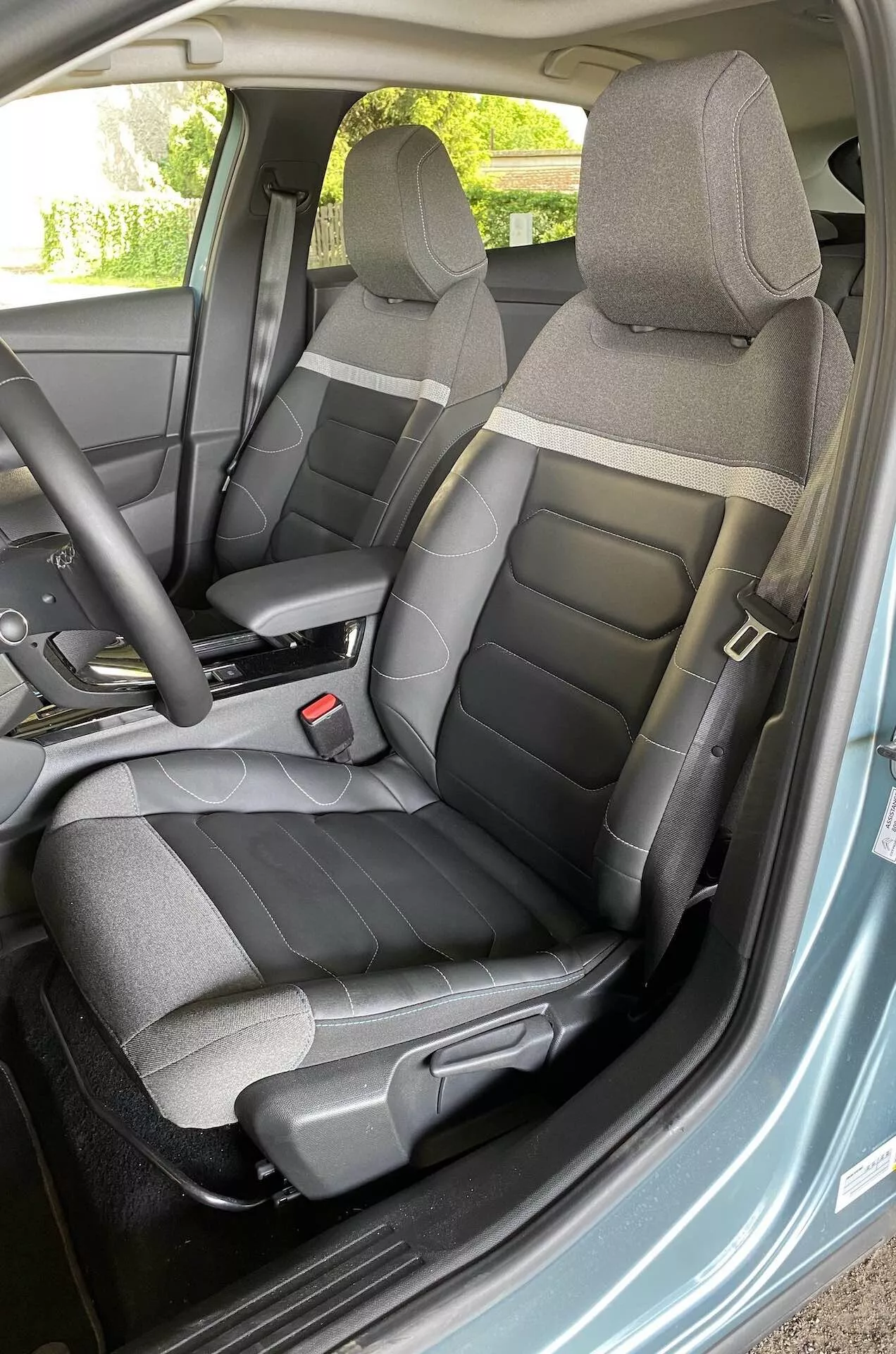 Vista interior do Citroen C4 2020 (e-C4) focando no lado do motorista, fotografada a partir do ângulo de uma porta aberta, mostrando o volante, os assentos e parte do painel com controles montados no volante.