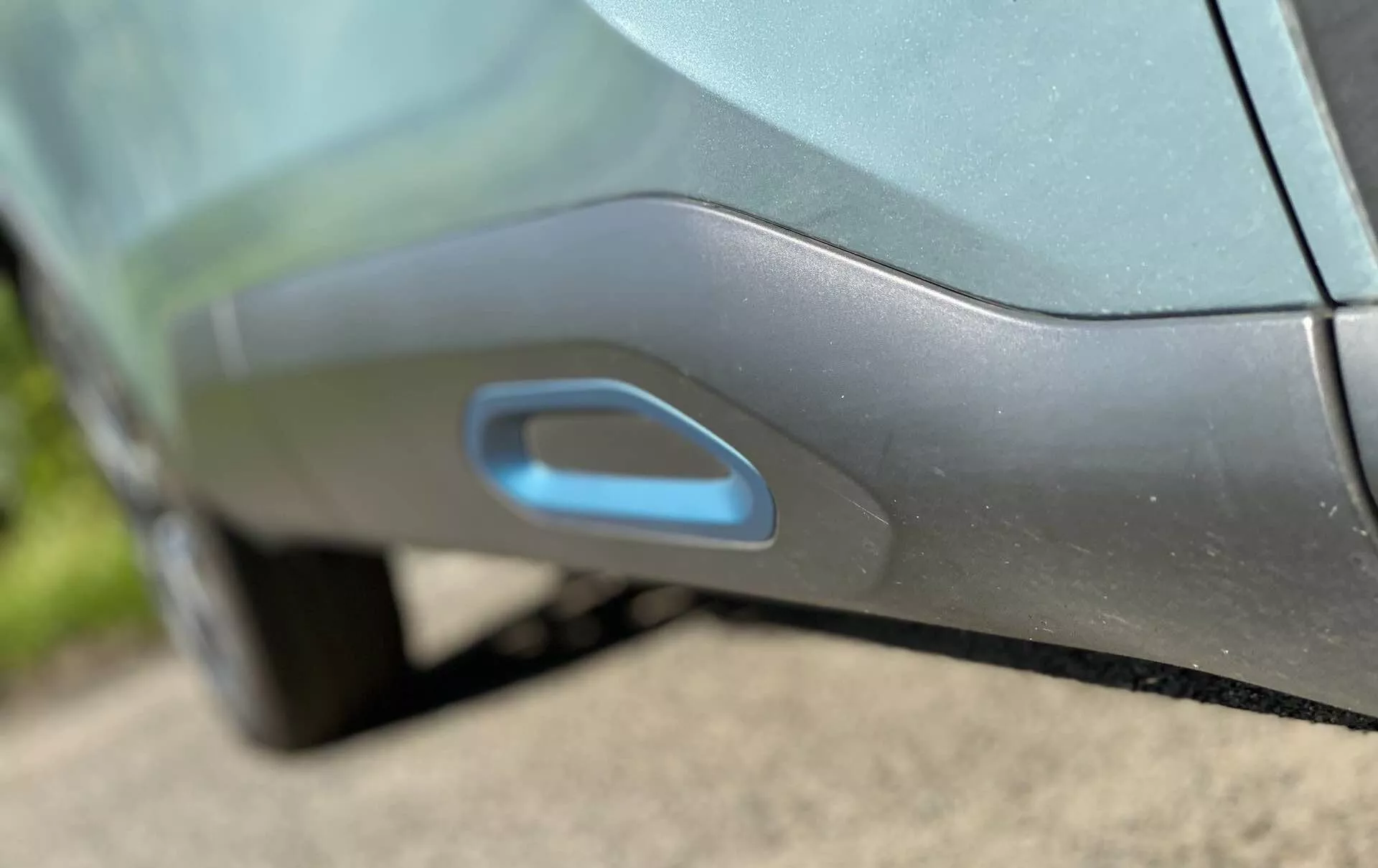 Close-up do detalhe lateral do Citroen C4 2020 (e-C4), destacando a moderna maçaneta integrada aerodinamicamente. A maçaneta está embutida no painel da porta, possivelmente iluminada para entrada sem chave, sugerindo um mecanismo avançado de deslizamento ou abertura eletrônica. A tonalidade metálica e o acabamento brilhante do carro são acentuados pelas sombras e reflexos da luz do dia.