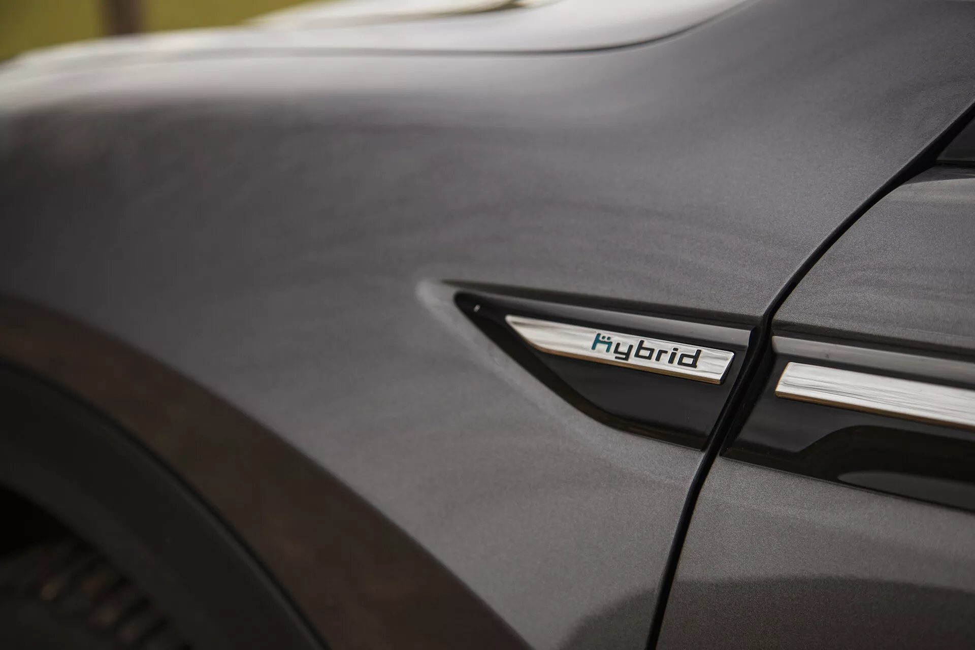 Detalhe em close-up do Citroen C5-X 2022 apresentando o emblema Híbrido no perfil lateral inferior próximo à caixa da roda traseira, destacando a tecnologia híbrida e a estética de design sob condições de iluminação suave