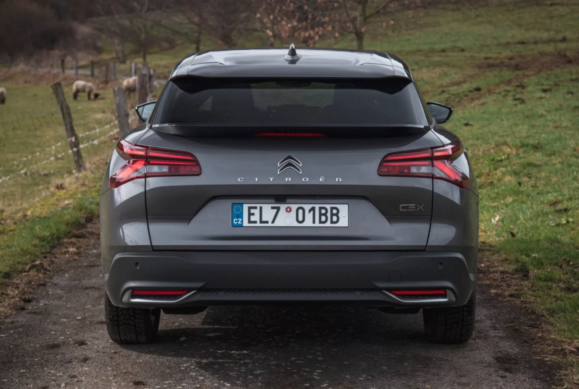 Vista traseira do Citroën C5X 2022 numa estrada de cascalho com fundo natural, exibindo lanternas traseiras LED, controle de distância de estacionamento, escape duplo e detalhes exteriores adicionais.