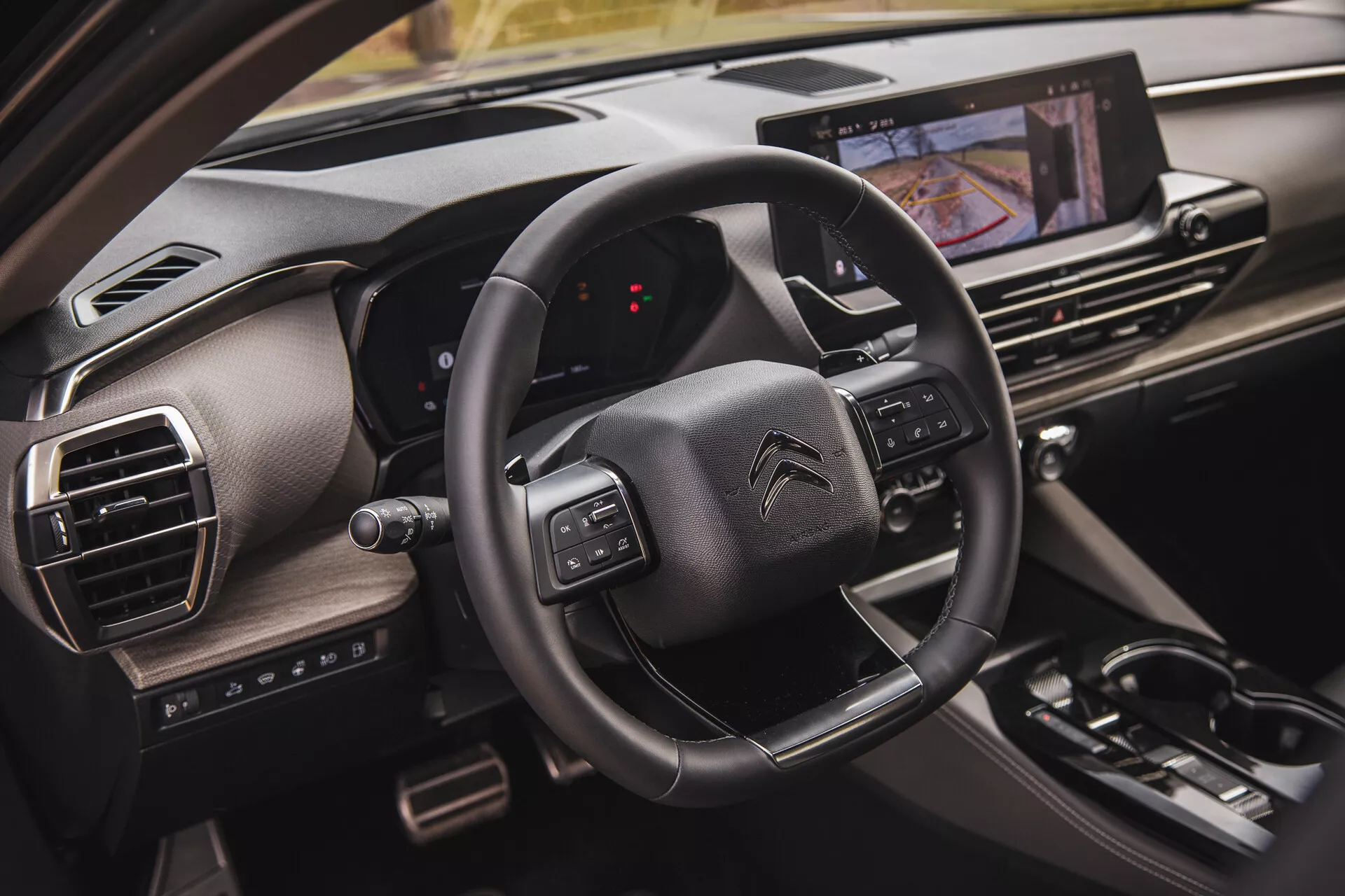 Vista aproximada do interior do Citroën C5-X 2022 mostrando o volante com botões multifuncionais, um display de dashboard digital a partir da perspectiva do passageiro, e um sistema de infotainment com tela sensível ao toque