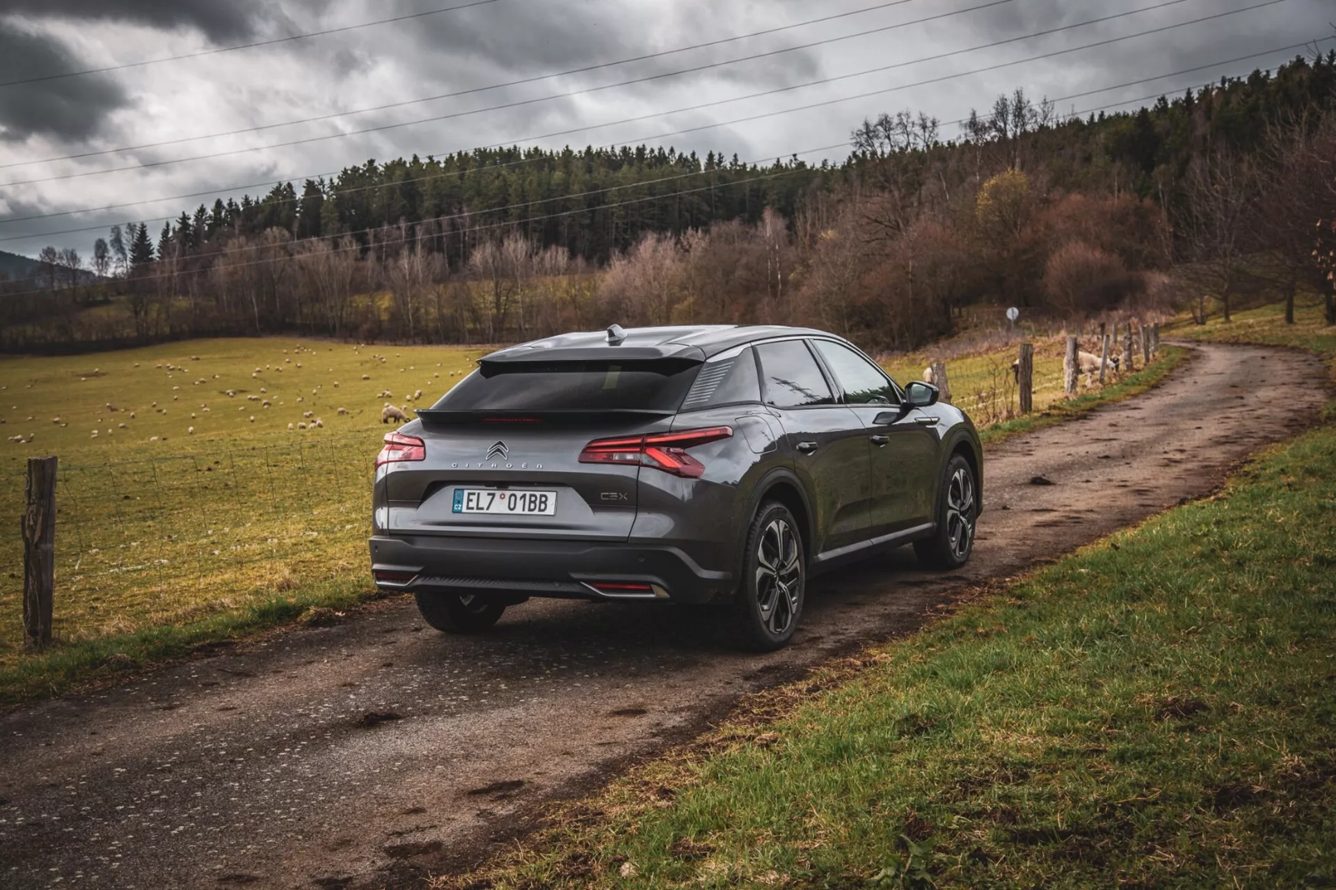 Citroen C5-X 2022 hatchback moderno estacionado numa estrada rural não asfaltada, visão traseira de três quartos exibindo design aerodinâmico com spoiler e antena em forma de barbatana de tubarão, luzes traseiras finas e horizontais e rodas grandes de múltiplos raios, sugerindo desempenho e luxo num ambiente extra-urbano.