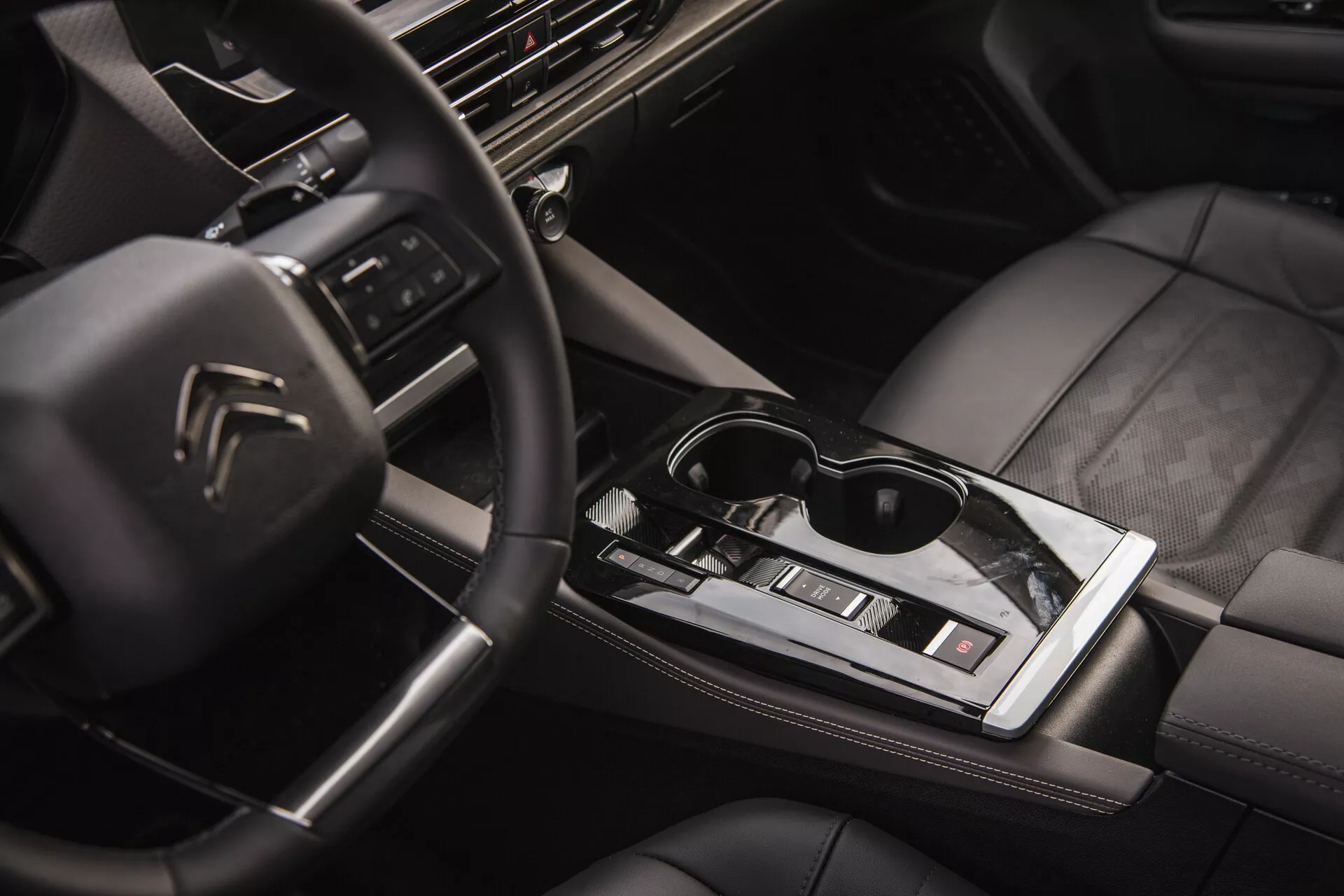 Vista interior do Citroën C5-X 2022 mostrando o volante multifuncional com logotipo, painel de alta tecnologia com sistema de infotainment, manopla de câmbio automático elegante, controle climático, assentos revestidos em couro com costura de qualidade e um toque de estilo de vida com óculos de sol na superfície central brilhante
