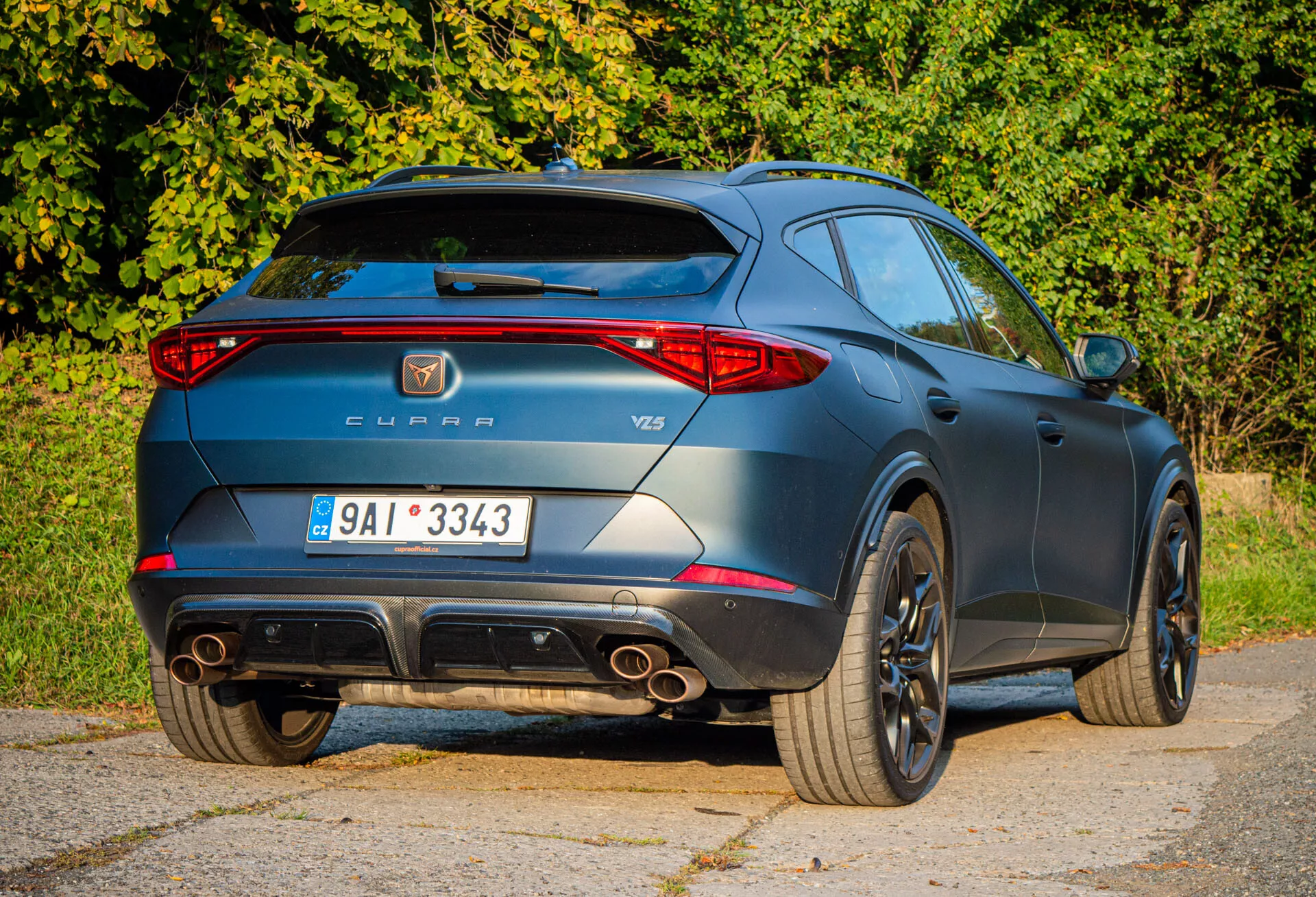 Vista traseira três quartos do Cupra Formentor 2020 destacando características esportivas como pontas de escape duplas, aerofólio de teto e rodas de liga leve, juntamente com a marcação do fabricante e modelo durante o dia