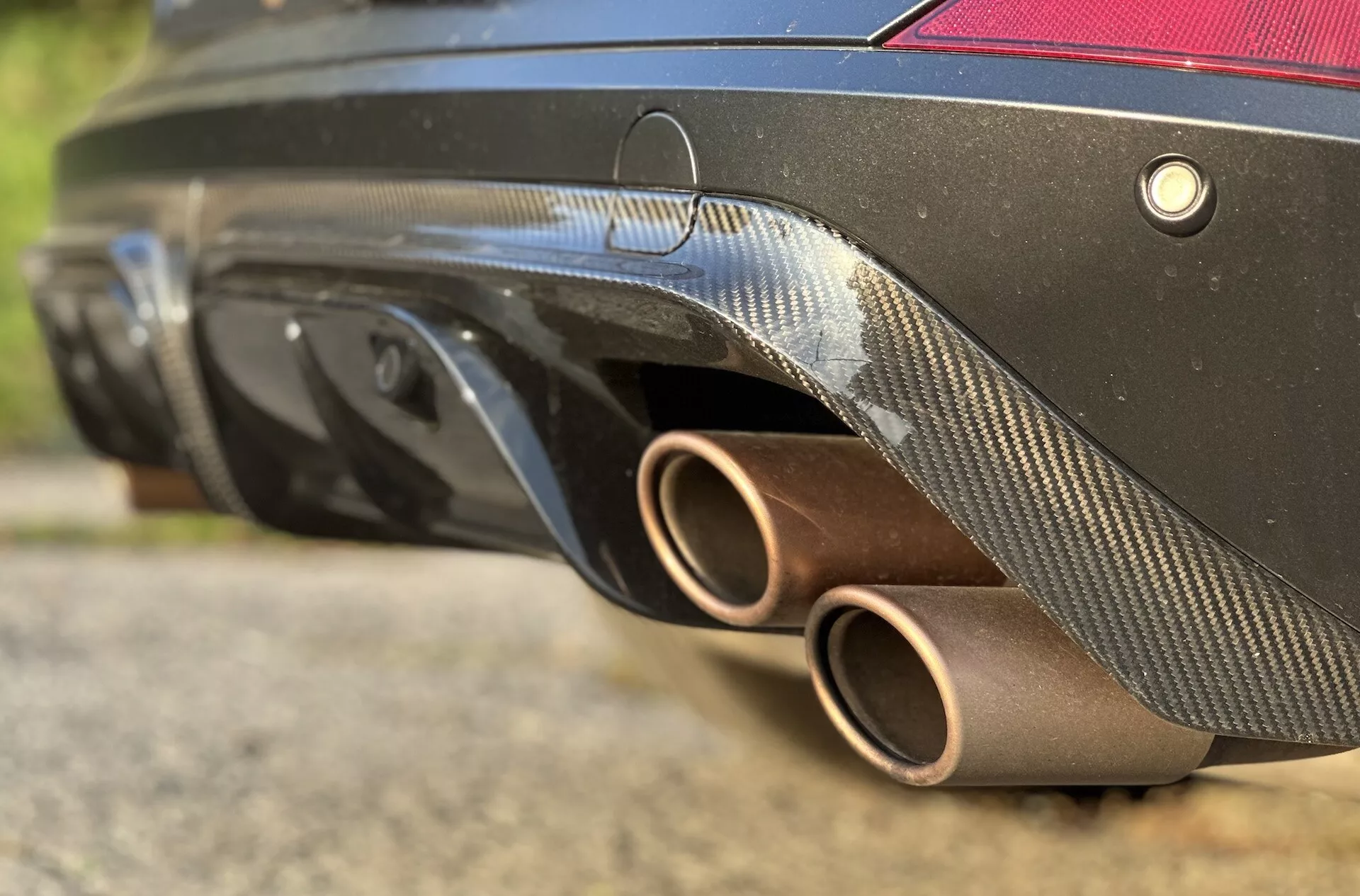 Vista de perto da traseira do Cupra Formentor 2020, destacando os tubos de escape bronze, difusor de fibra de carbono, sistema de sensores e cor preta da carroceria de um ângulo baixo, enfatizando seu design esportivo e características de desempenho