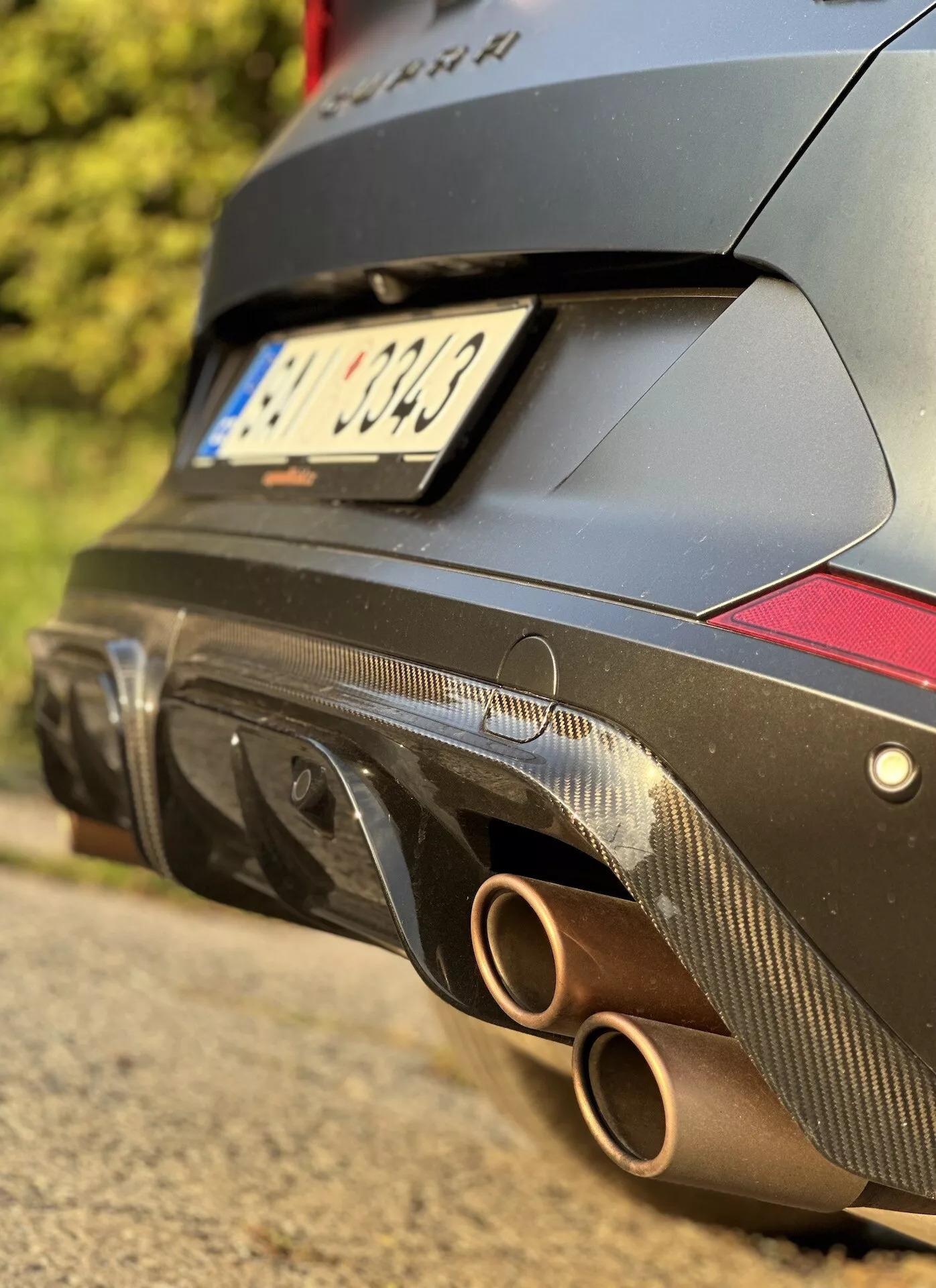 Vista detalhada da seção traseira do Cupra Formentor 2020 focando no sistema de escape com dupla saída redonda e difusor em fibra de carbono com refletores vermelhos, contra um corpo de design de performance de cor escura.