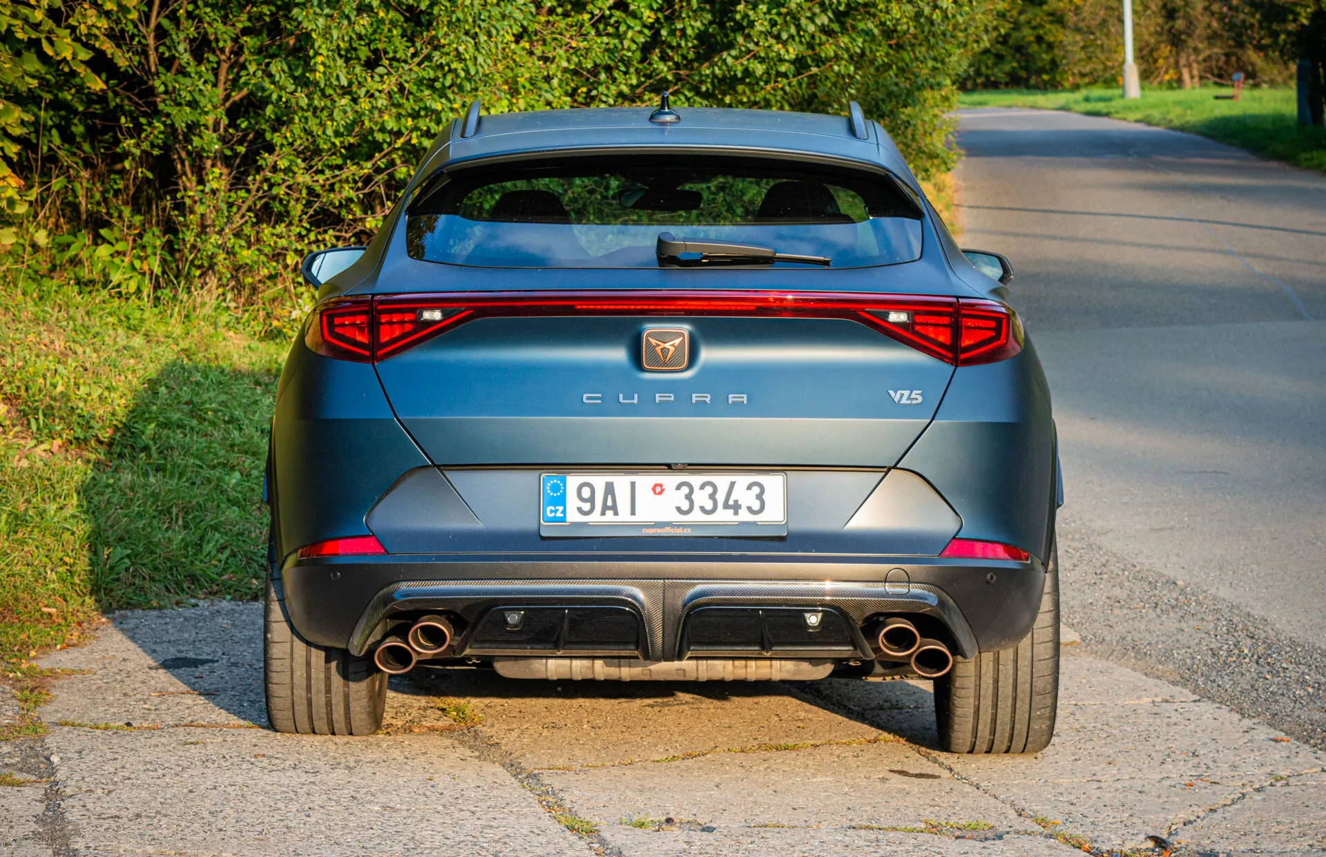 Vista traseira de um CUPRA Formentor VZ5 de 2020 em cinza metálico estacionado ao lado da estrada, exibindo faróis traseiros LED, escapamentos duplos e características de design aerodinâmico durante uma captura de luz diurna no final da tarde