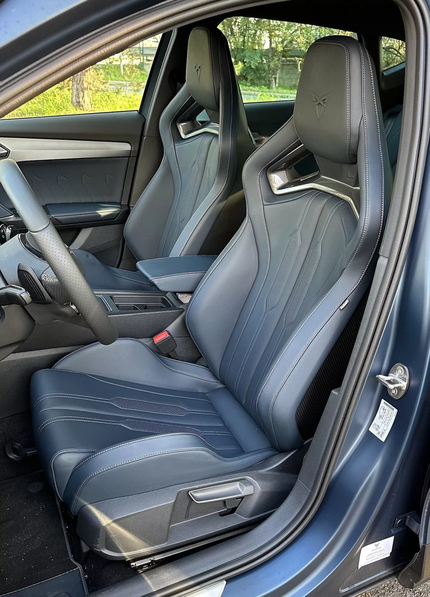 Vista do interior de um Cupra Formentor 2020 mostrando o assento do motorista de um ângulo de três quartos, com porta aberta, bancos esportivos com costura azul clara, e um vislumbre do console central e painel de instrumentos.