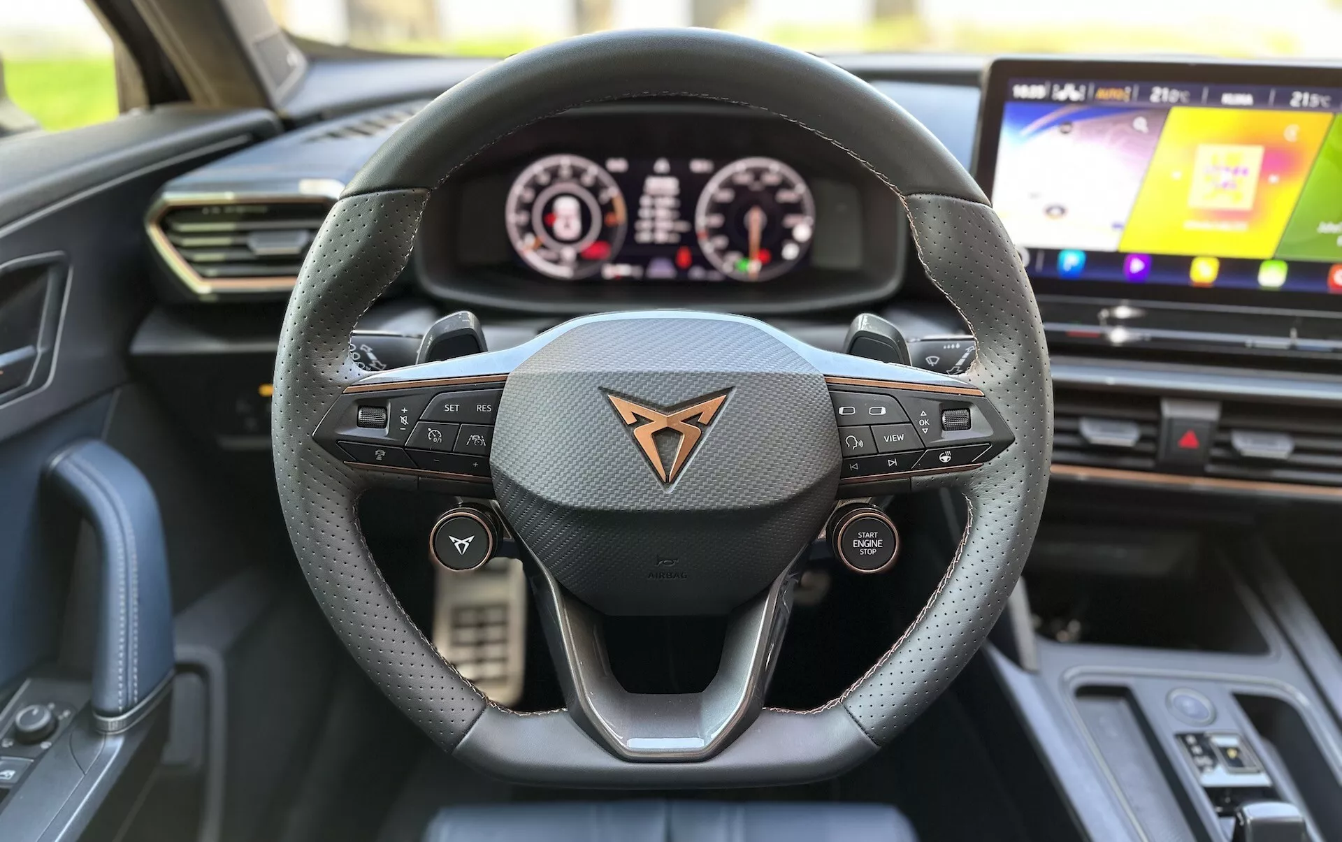 Vista interior de um Cupra Formentor 2020 a partir do ponto de vista do assento do condutor, destacando o volante revestido a couro de três raios com botões multifuncionais, um painel de instrumentos digital e sistema de infotenimento touchscreen.