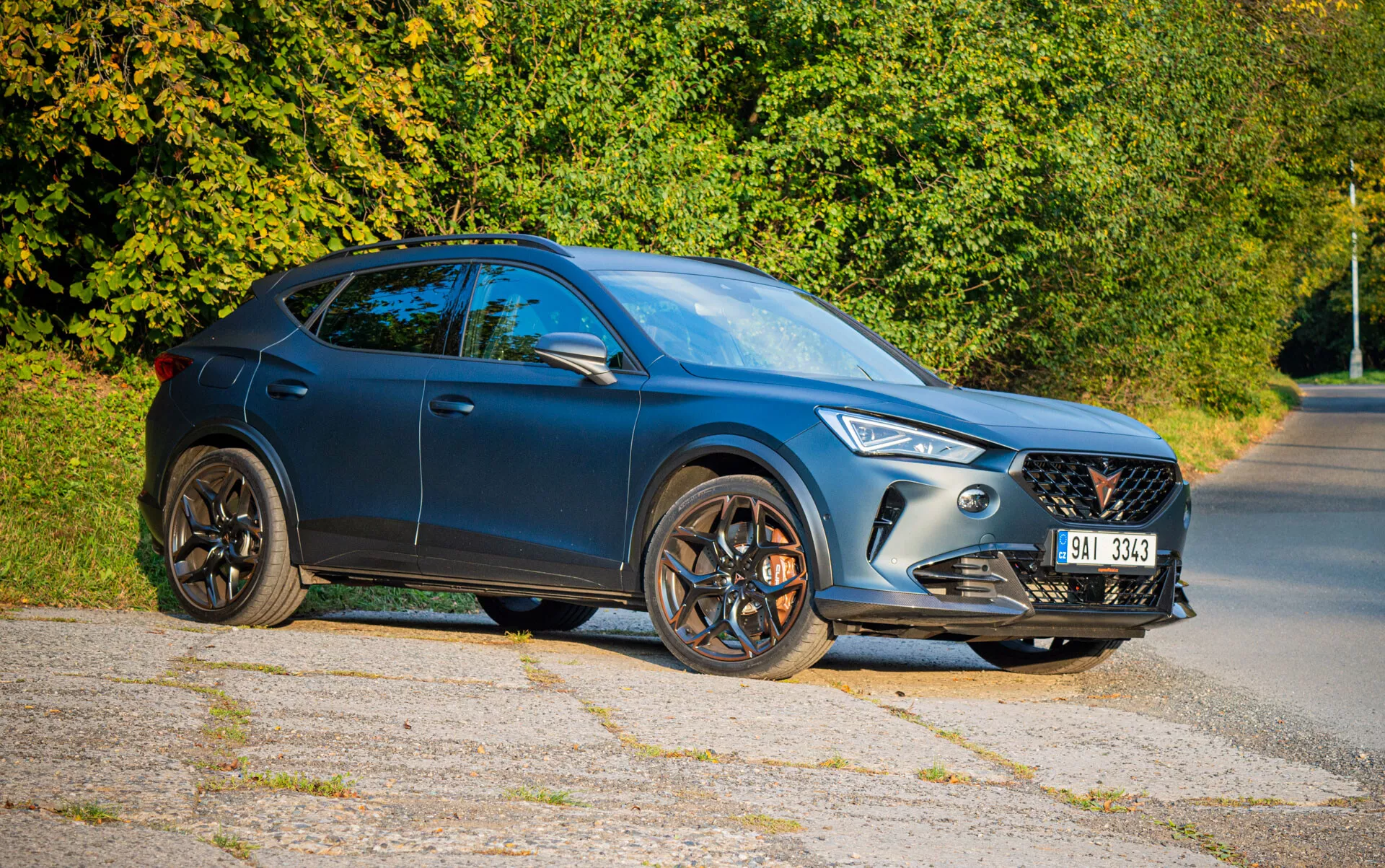 SUV crossover Cupra Formentor 2020 em azul escuro, com design elegante, faróis LED e rodas de liga leve de cinco raios, fotografado de um ângulo frontal de três quartos numa estrada suburbana