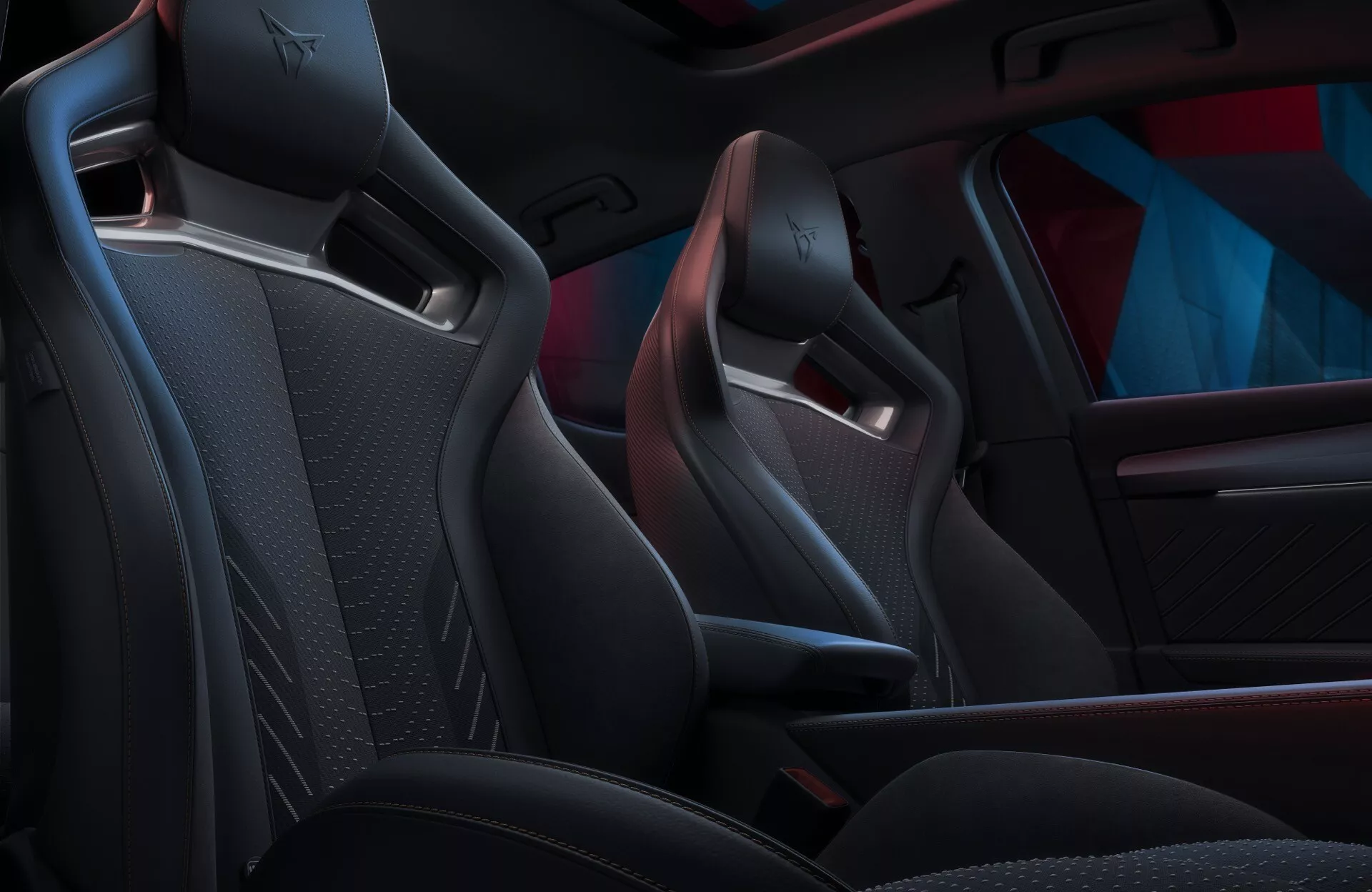 Interior do Cupra Leon 2024 facelift de primeira geração, com bancos dianteiros esportivos revestidos em material escuro de alta qualidade com um logotipo em relevo proeminente, iluminado por luz de ambiente personalizável em vermelho e azul.