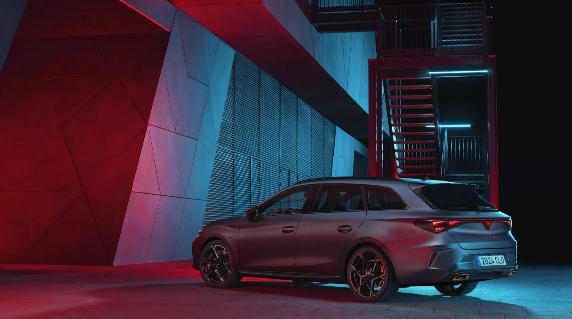 Cupra Leon 2024 primeira geração facelift fotografado de um ângulo traseiro de três quartos, destacando o lado do passageiro. Iluminação noturna dramática enfatiza características de design do carro incluindo faróis traseiros esportivos, para-choque traseiro, agressivo spoiler de teto e rodas voltadas para desempenho em um pano de fundo urbano e industrial.