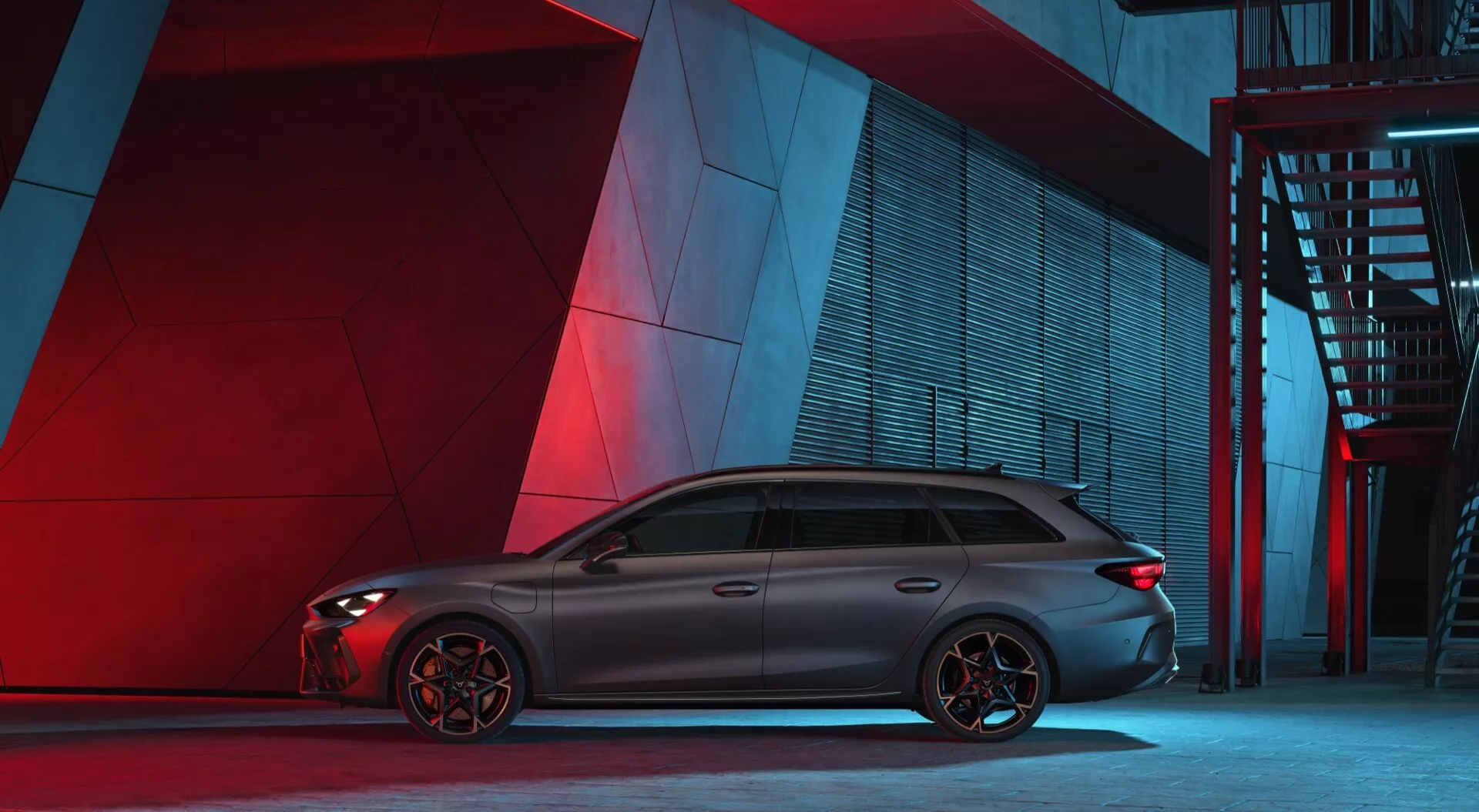 Vista de perfil lateral do Cupra Leon 2024 desportivo e elegante numa ambiente urbano noturno com iluminação artificial vermelha e azul ao fundo. O carro apresenta uma silhueta longa e aerodinâmica com janelas escuras e acabamentos cromados, uma linha do teto que termina com um spoiler e rodas de liga leve distintas com vários raios. As pinças de freio visíveis sugerem freios orientados para desempenho. A carroçaria tem linhas contornadas e não existem emblemas ou características tecnológicas facilmente identificáveis ​​a partir deste ângulo.