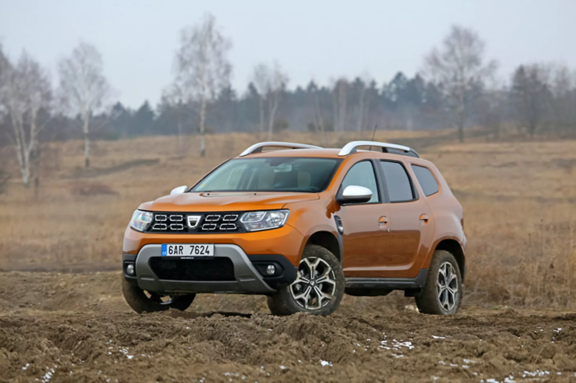 SUV compacto Dacia Duster 2013 exibido em um cenário externo, off-road, destacado por sua cor laranja distinta, altura elevada do passeio, rodas de liga leve e revestimento de corpo de plástico para uso leve fora de estrada, capturado de um ângulo frontal de três quartos.