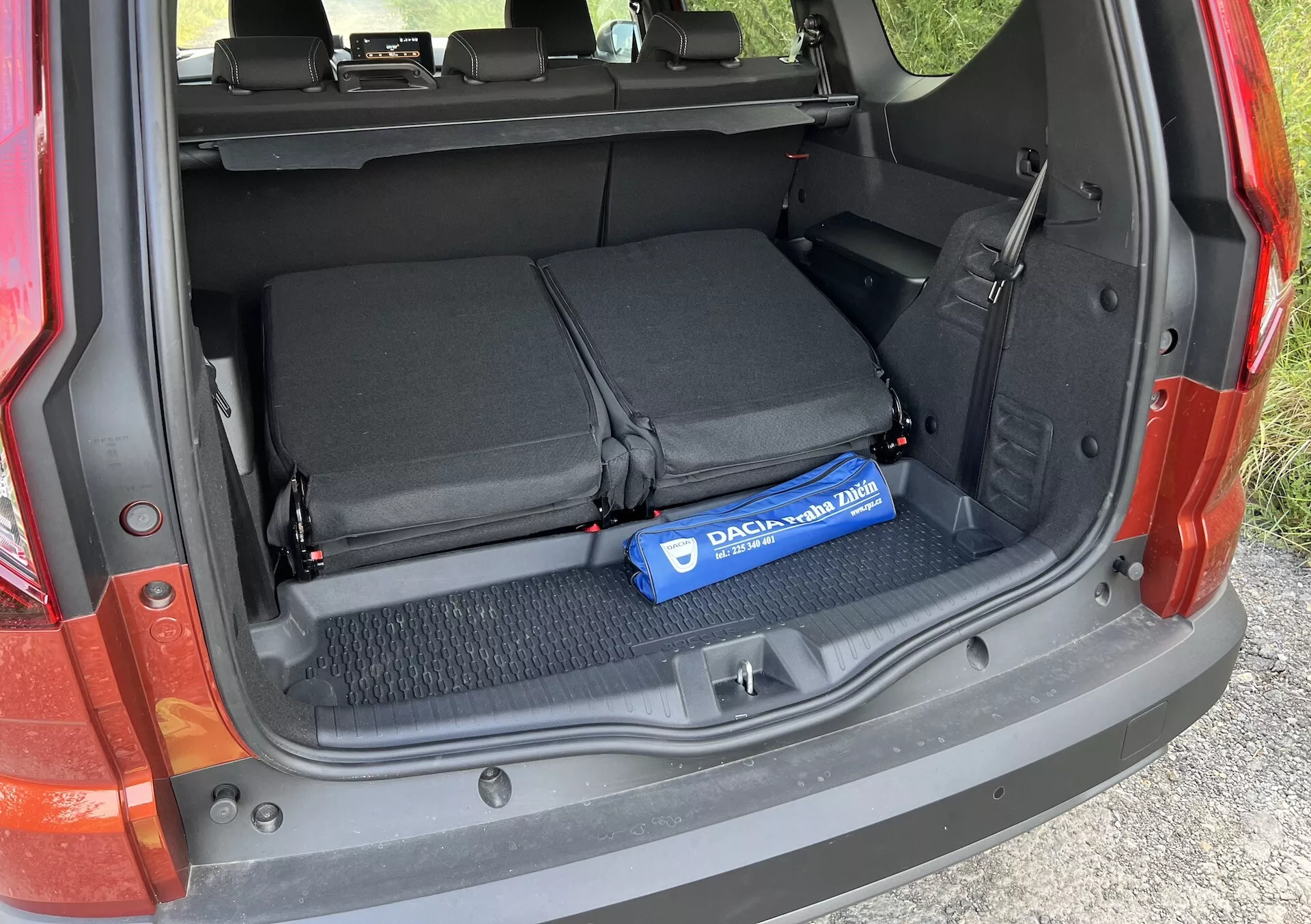 Detalhe do porta-malas do Dacia Jogger 2022 mostrando a área de carga aberta com os bancos traseiros dobrados, laços têxteis para segurar itens e um cilindro azul Decaux no chão carpetado