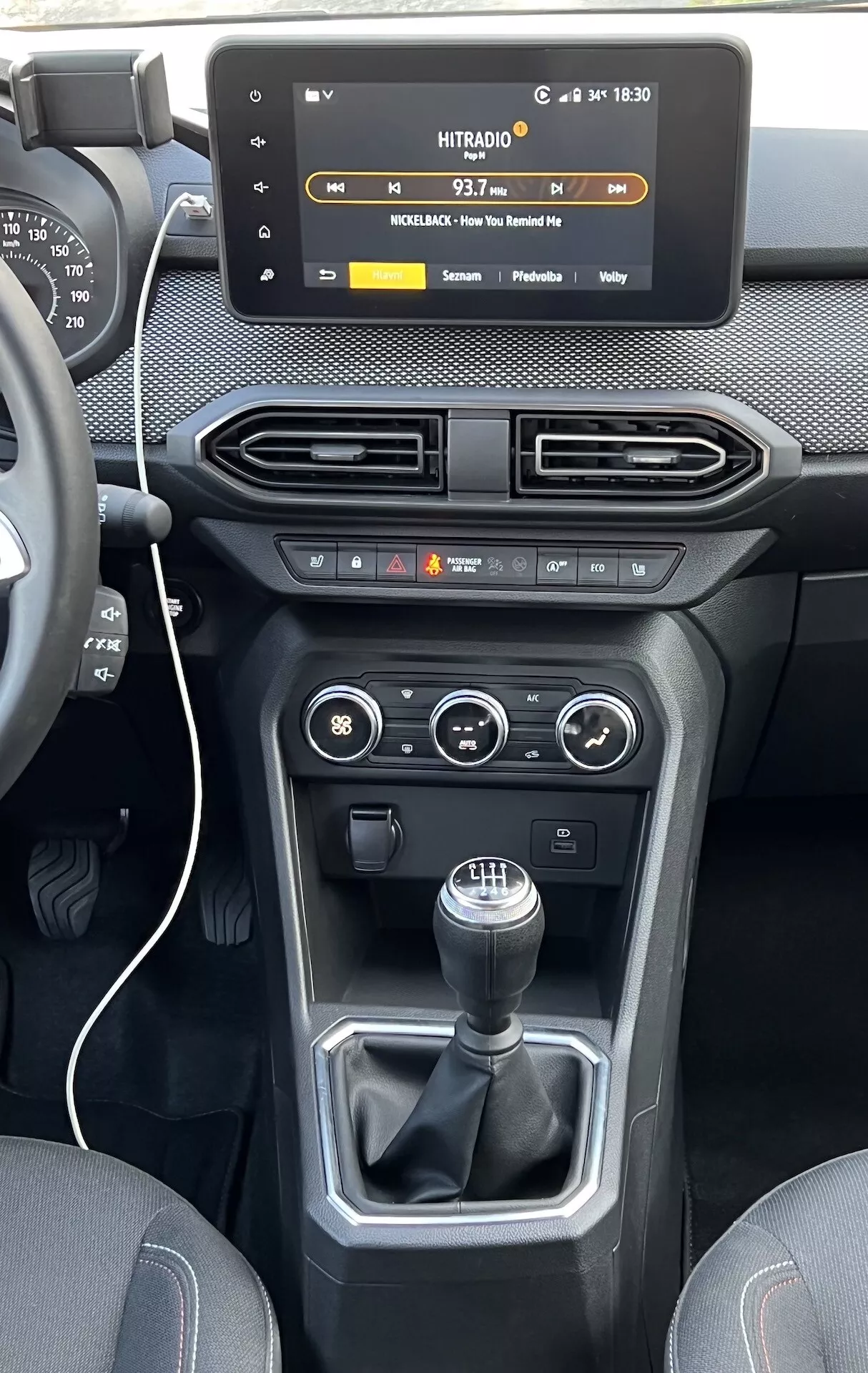 Vista interior do Dacia Jogger 2022 com foco no console central e painel de instrumentos, apresentando uma tela sensível ao toque flutuante de infotenimento, saídas de ar, controles de clima e do veículo, e uma alavanca de câmbio manual