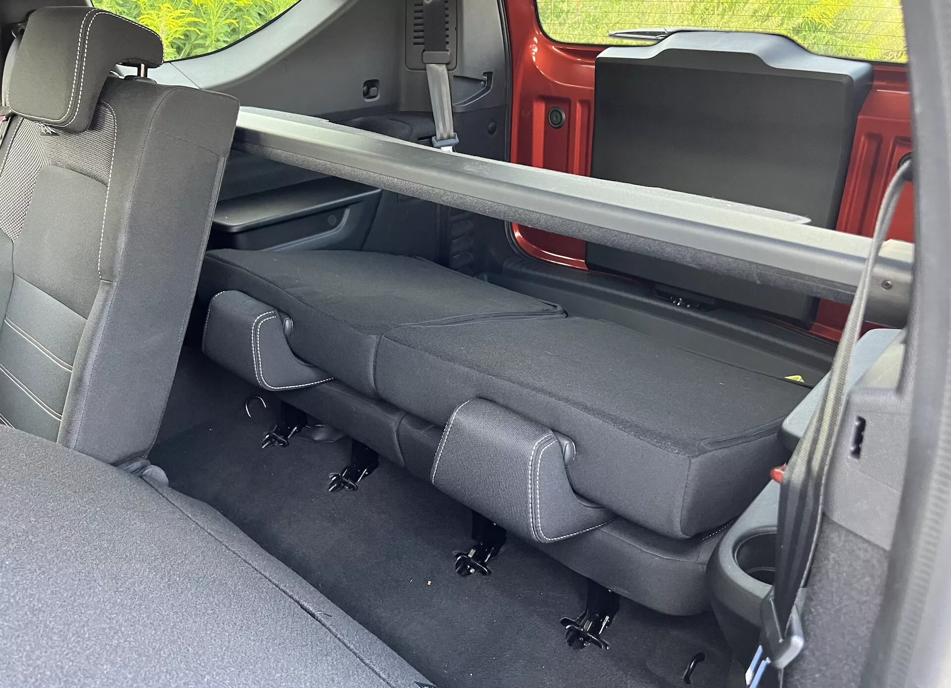 Vista interior do Dacia Jogger 2022 focada no compartimento de passageiros traseiro com estofamento escuro, cintos de segurança retráteis, sistema LATCH e mecanismo de bancos dobráveis, vista pela porta traseira do lado do passageiro.