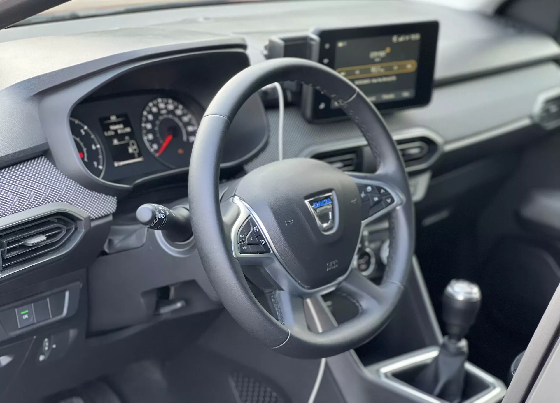 Vista interior do Dacia Jogger 2022 focada na área do condutor com volante multifuncional de três raios, painel de instrumentos analógico-digital, consola central com sistema de infotainment e alavanca de câmbio manual