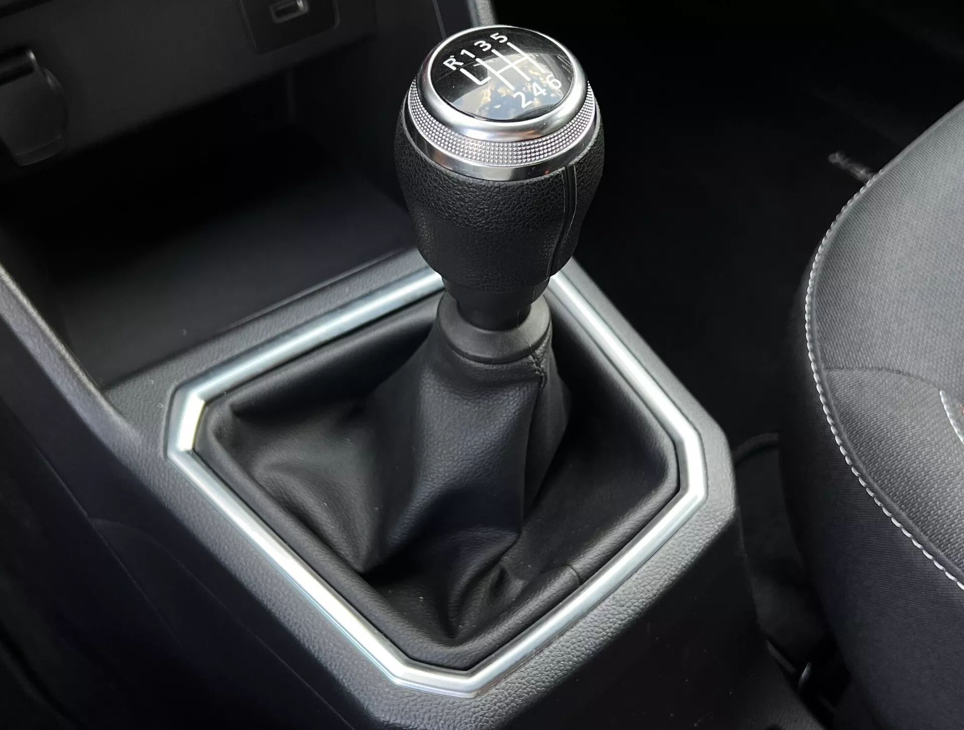 Vista detalhada do seletor de mudanças de transmissão manual Dacia Jogger 2022, exibindo um padrão de mudança de 6 velocidades, alavanca coberta de couro e inserção metálica hexagonal em um interior de carro refinado