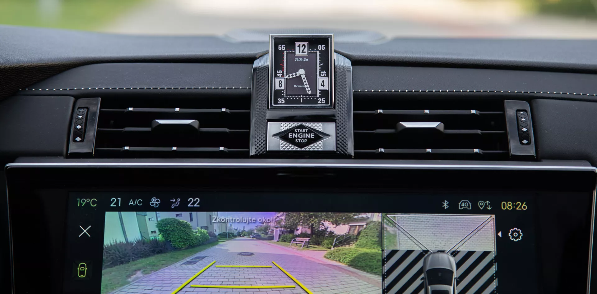 Vista interior do DS Automobiles DS-7 2022 mostrando o painel de instrumentos, relógio analógico de luxo, e display do sistema central de infotenimento com câmera traseira e recurso de assistência ao estacionamento