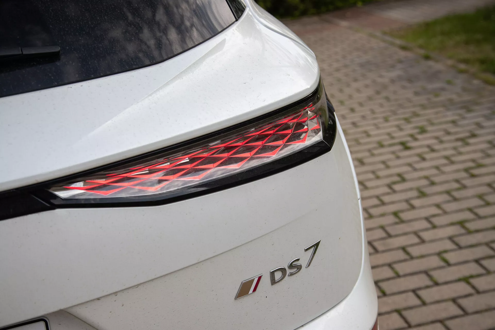 Close-up da seção traseira do DS 7 branco mostrando lanterna traseira LED moderna e emblema do modelo, destacando detalhes de design e acabamento premium