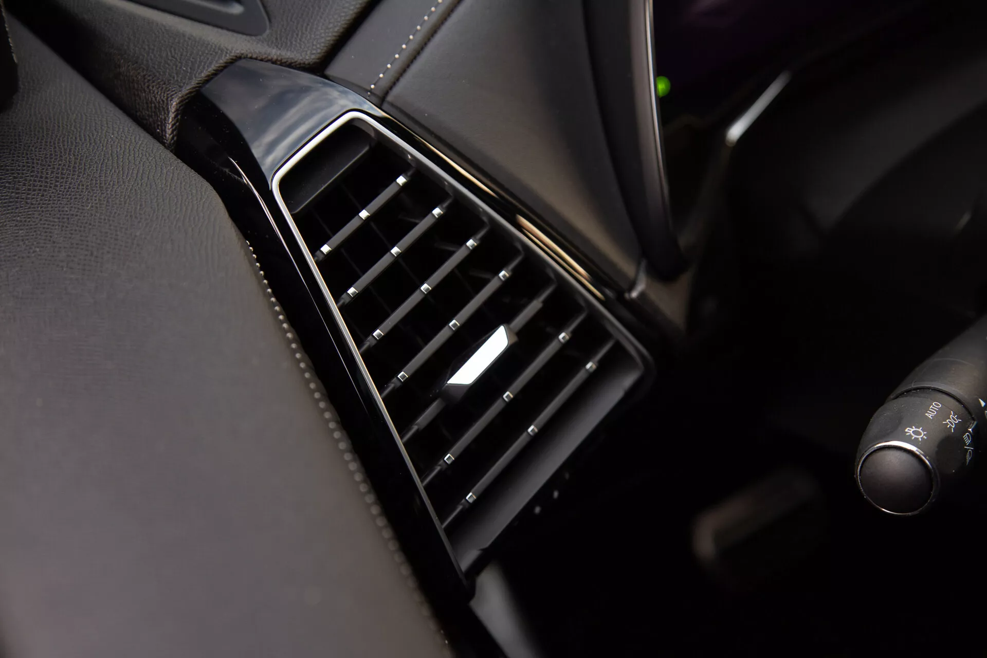 Vista de perto do respiradouro do DS Automobiles DS-7 2022 no painel com palhetas ajustáveis pretas alinhadas verticalmente, moldura brilhante e um toque de prata no controle, evidenciando a qualidade do design interior e dos materiais do veículo
