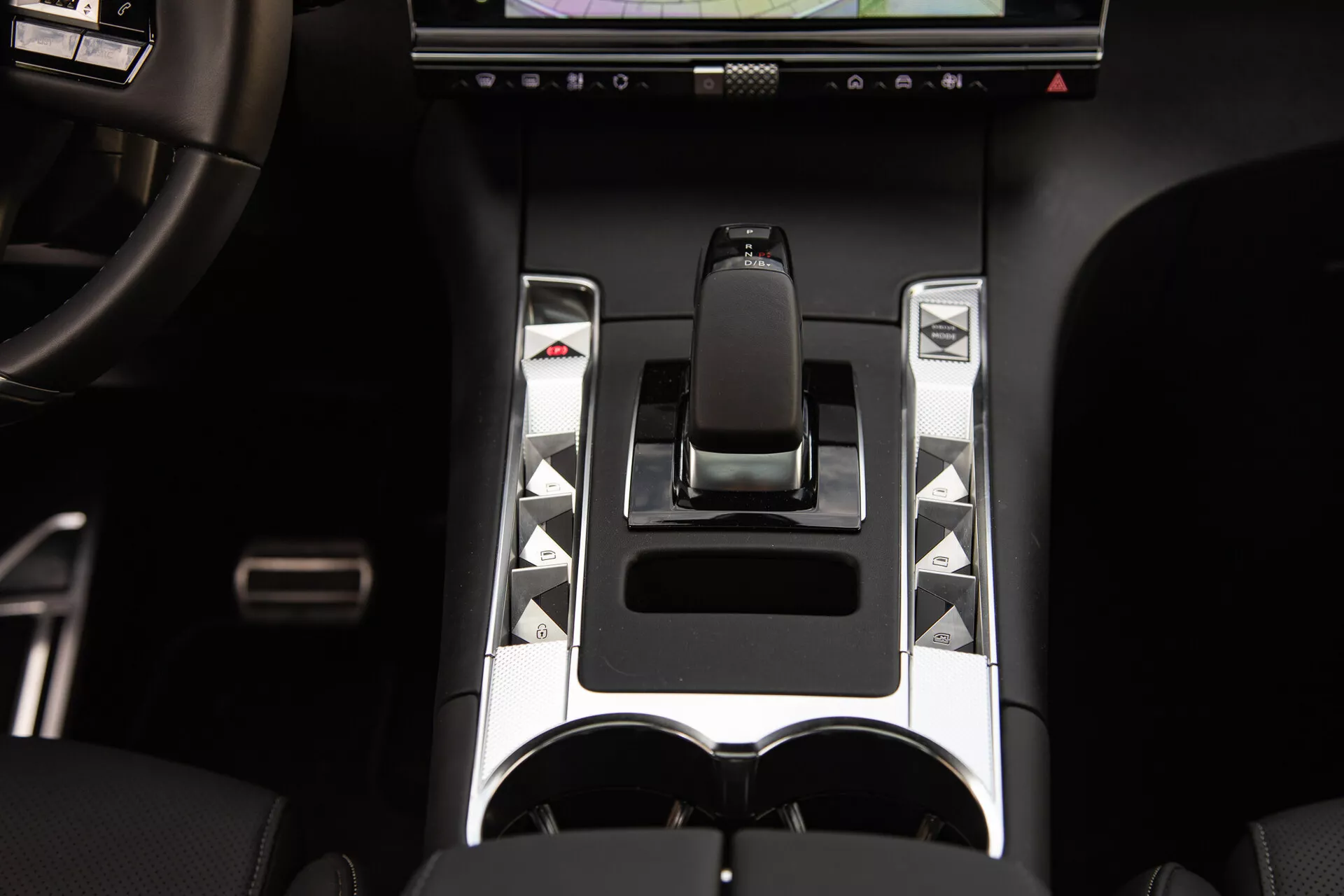 Vista detalhada do console central do DS Automobiles DS-7 2022 com alavanca de câmbio ergonômica, destaques metálicos, botões de controle únicos, tela sensível ao toque e porta-copos duplo, destacando elementos avançados de controle de veículo e elementos de design de luxo.