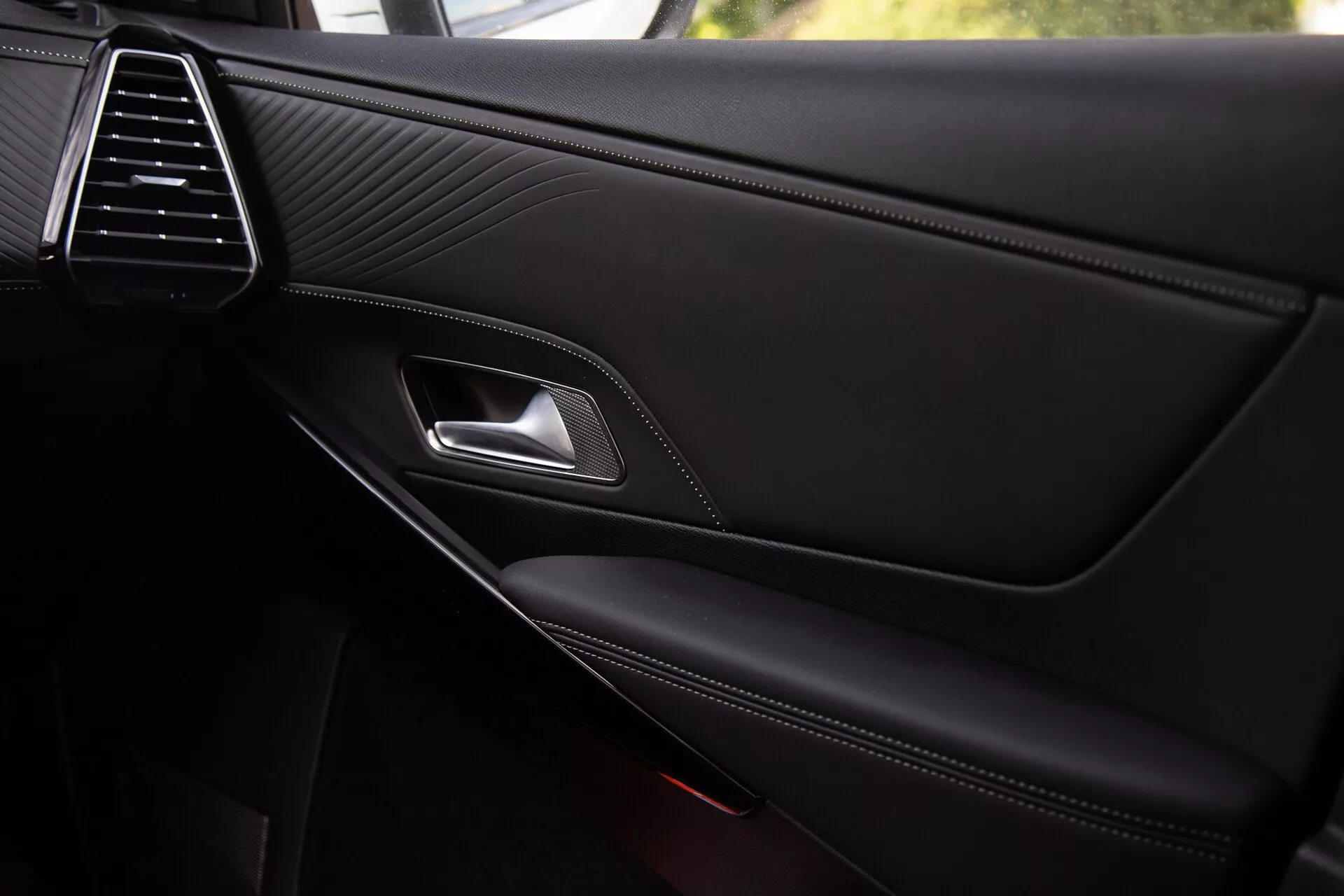 Visão detalhada do painel da porta interior do DS Automobiles DS-7 2022, apresentando a elegante saída de ar, textura de couro costurado, puxador da porta cromado, alavanca de trava ergonômica, apoio de braço com costura contrastante e bolso de armazenamento integrado com grade do alto-falante parcialmente visível, refletindo qualidade premium e detalhes de design.