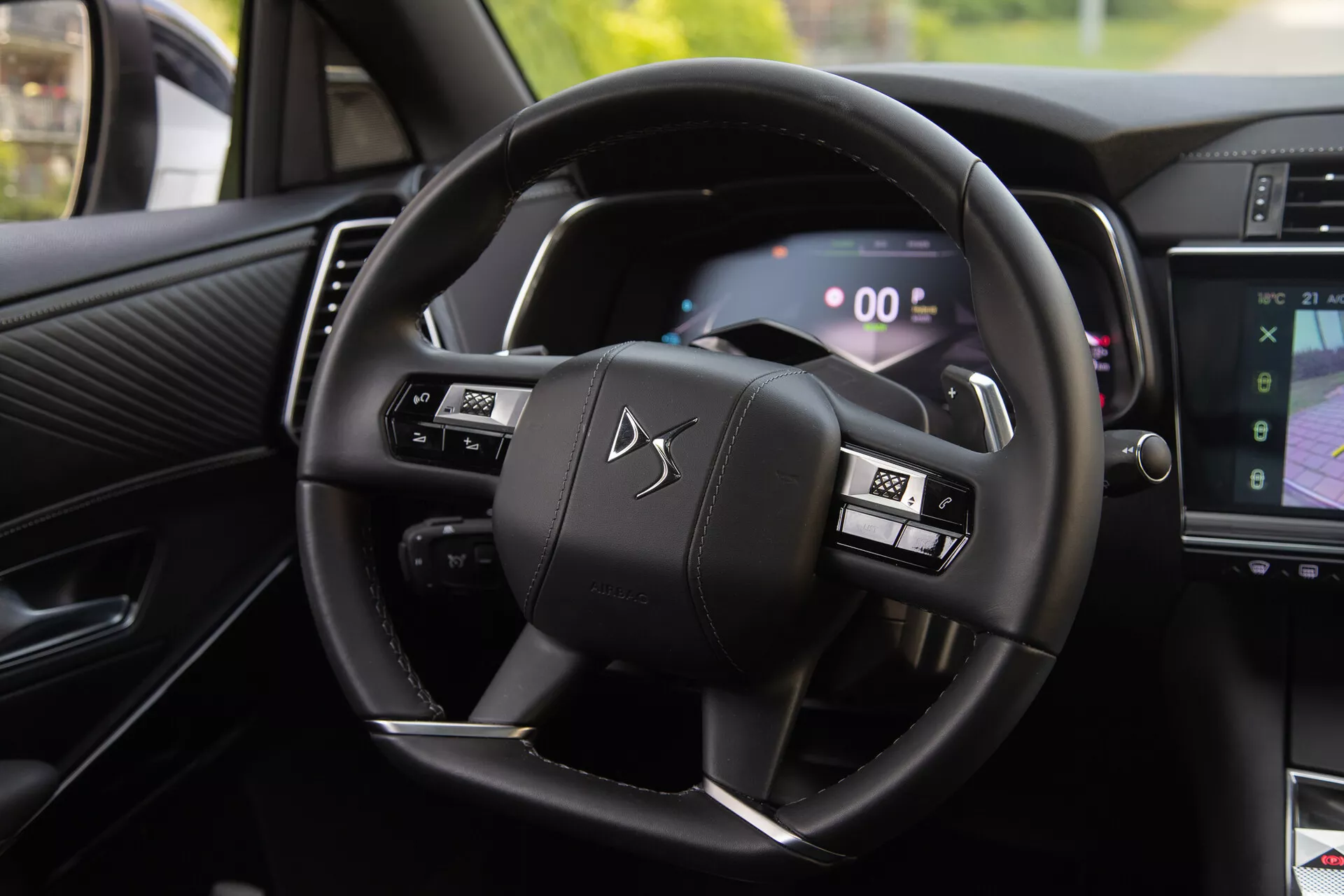 Vista interior do DS Automobiles DS-7 2022 mostrando o volante com botões multifuncionais e o painel de instrumentos digital, incluindo shift paddles e parte do sistema de infotenimento mostrando navegação