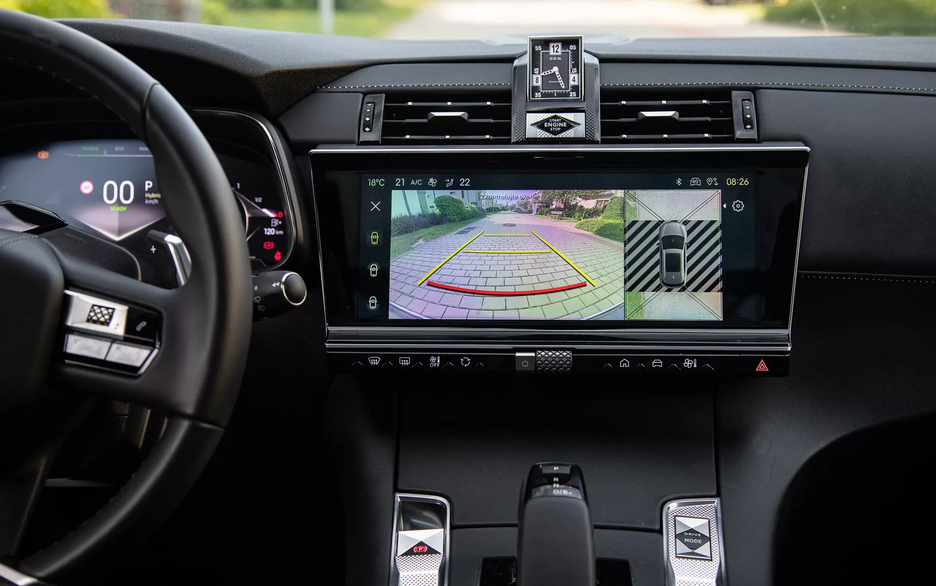 Detalhe do interior luxuoso do DS-7 2022 exibindo sistema de infotainment com display de câmera de ré e guias dinâmicas de assistência ao estacionamento, saídas de ar central, botões de controle de clima, alavanca de câmbio esportiva e velocímetro digital