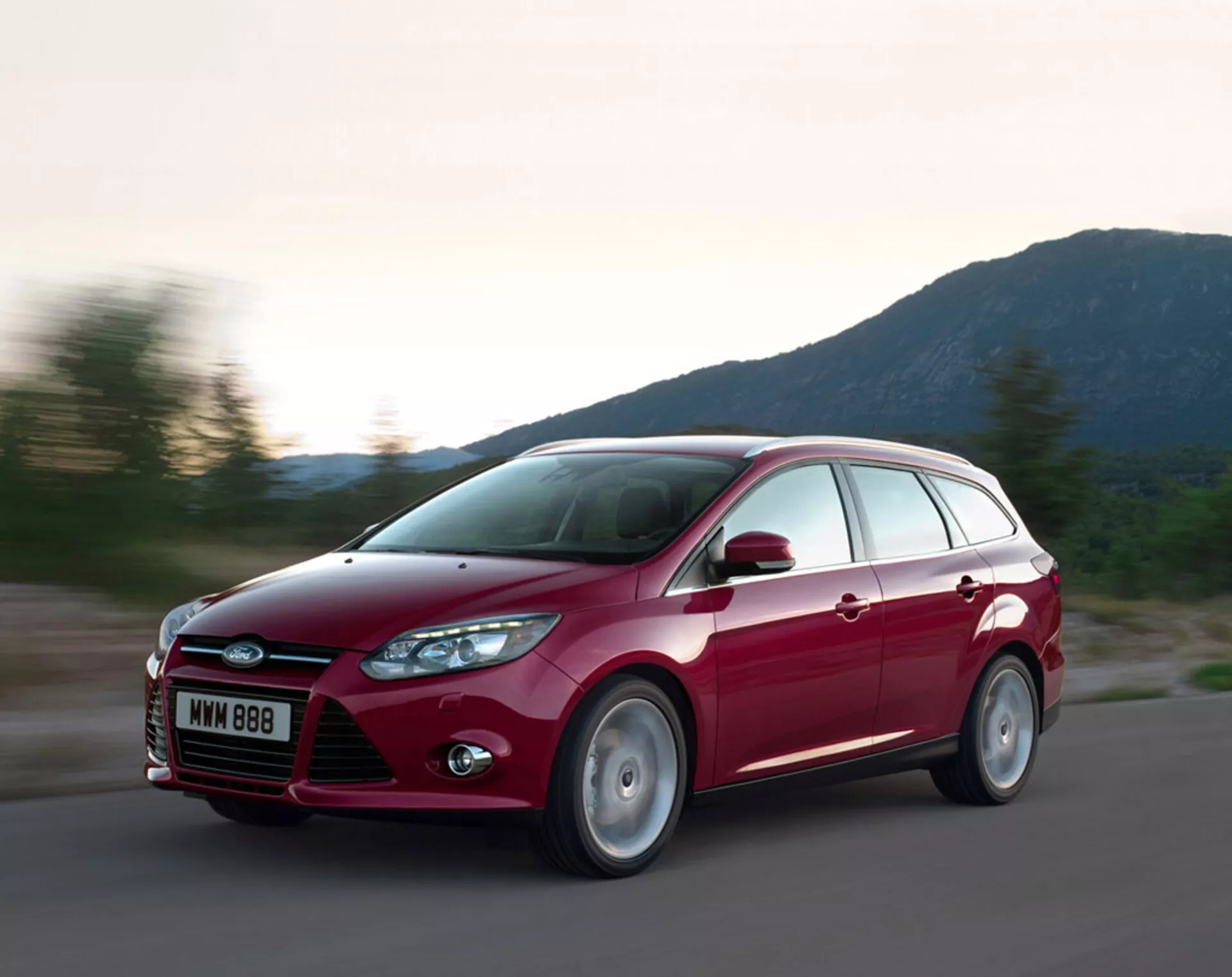 Ford Focus station wagon vermelho de 2011 em movimento em uma estrada de asfalto, exibindo seu design moderno, grade frontal proeminente com logo da Ford, faróis recuados, linhas esculpidas no capô e rodas de liga leve, sob condições de iluminação noturna